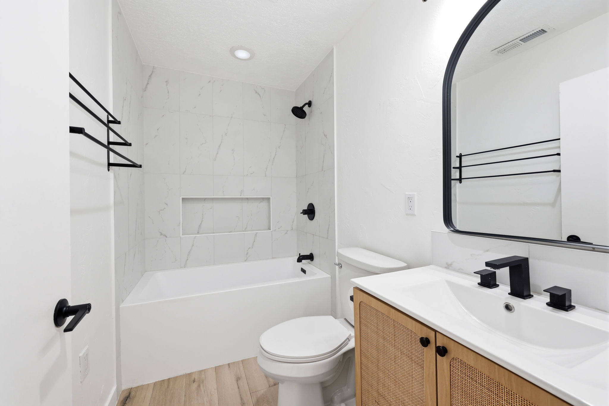 Bathroom featuring a white bathtub with a tiled surround, a built-in shower niche, and matte black fixtures