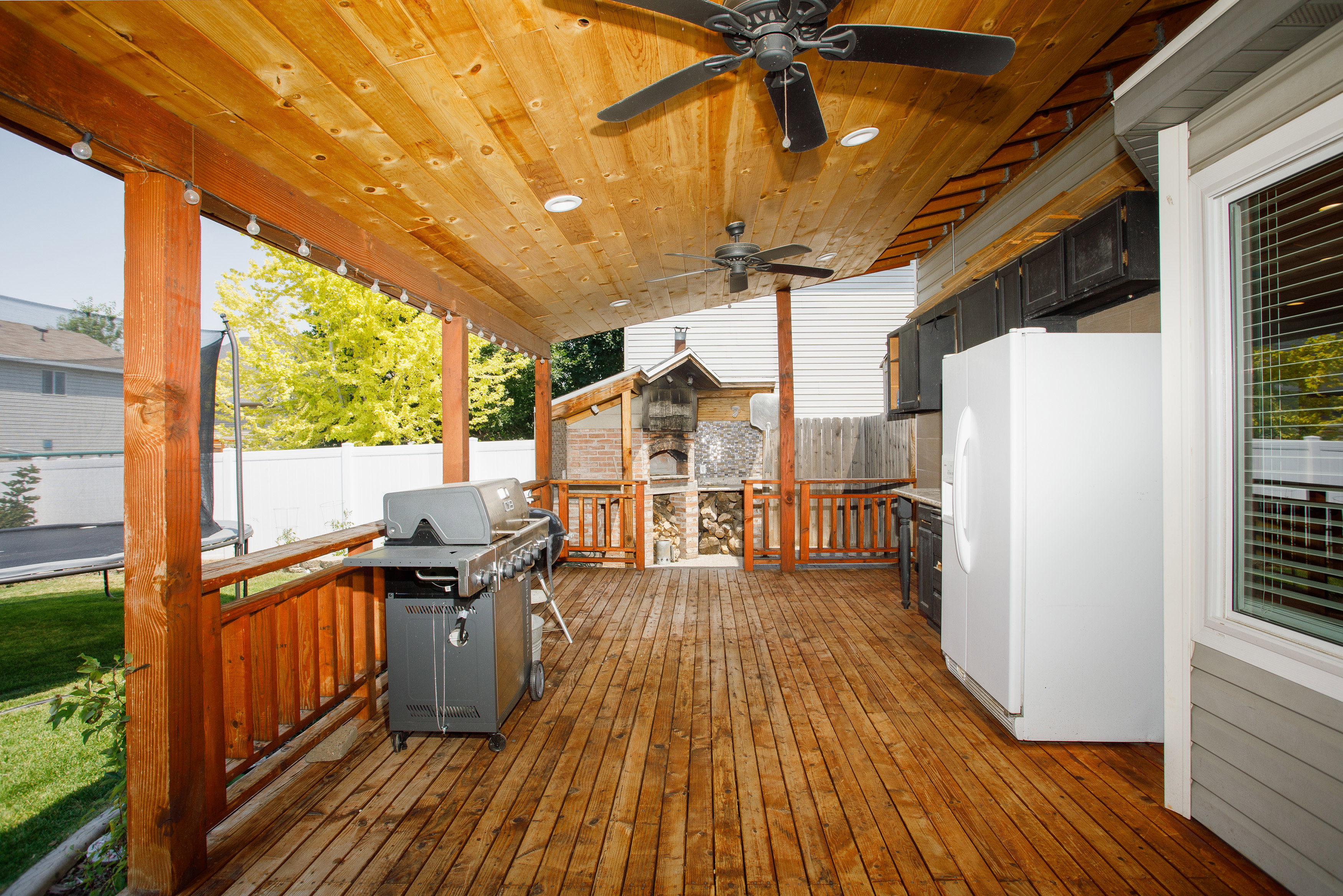 Expansive covered deck featuring wood-finish flooring, a wood-plank ceiling with recessed lighting and ceiling fans, and built-in cabinetry