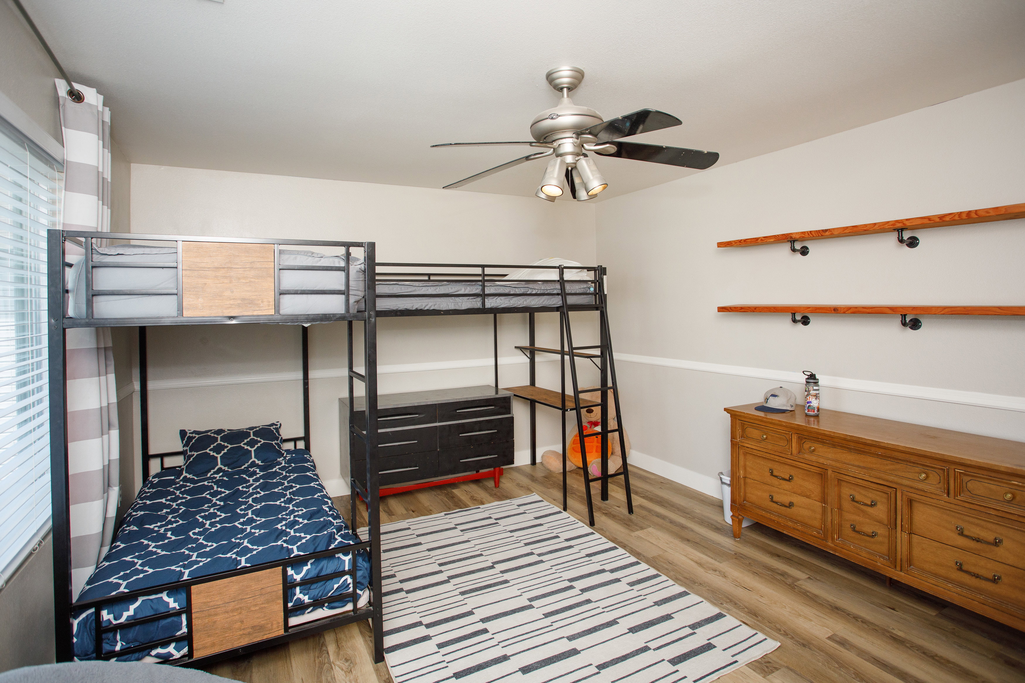 Room featuring light wood-finish flooring, a ceiling fan with integrated lighting, and horizontal wall shelving