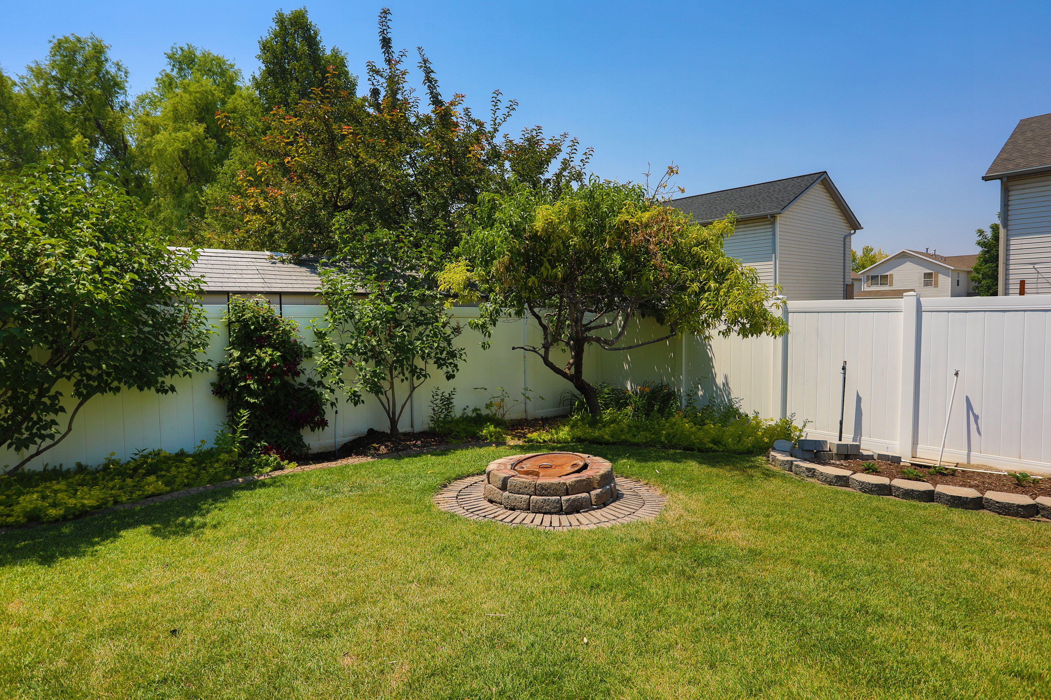Expansive backyard featuring a stone-ringed fire pit, manicured lawn, and mature trees