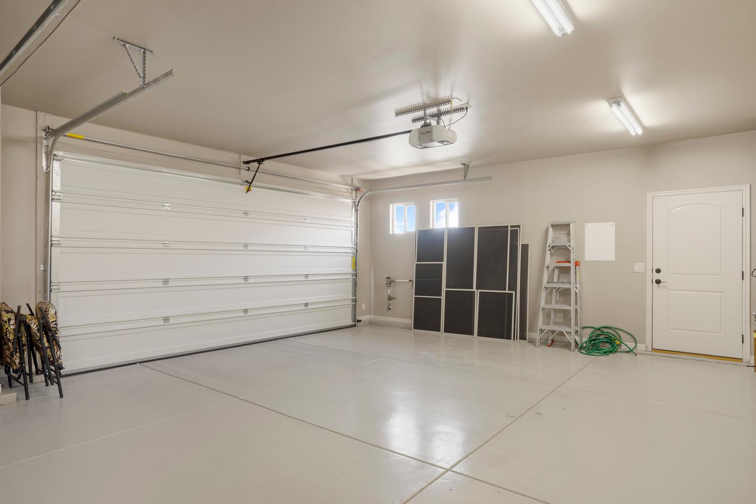 Two-car garage featuring a sectional garage door, epoxy-coated concrete flooring, two transom windows, recessed lighting, and a side access door