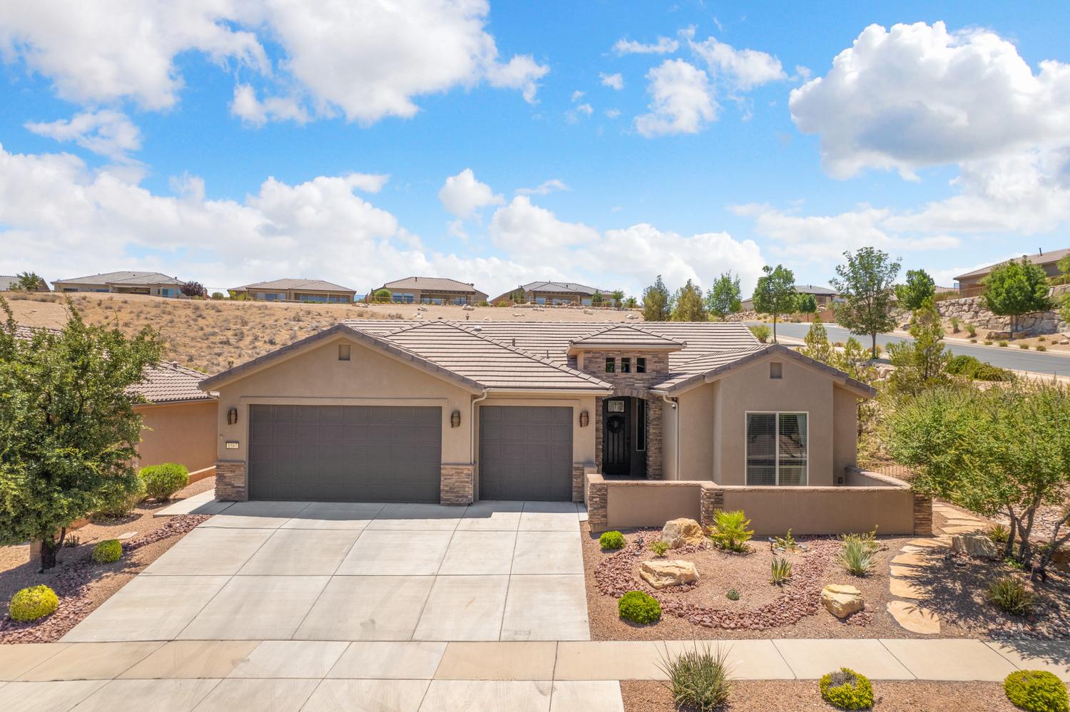 Contemporary stucco and stone-accented home featuring a concrete driveway, two-car garage, tile roof, and desert-style landscaping
