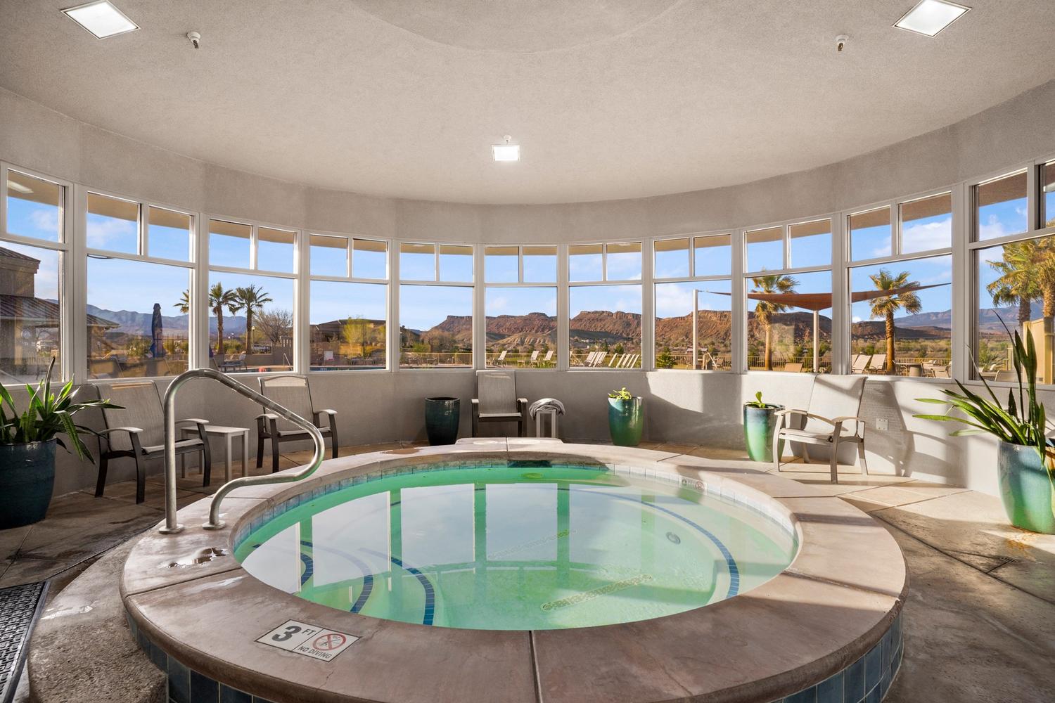 Circular indoor spa with a stone surround and integrated handrails, set within a curved room featuring a panoramic wall of windows