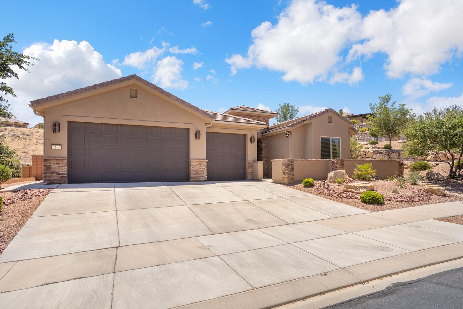 Stucco exterior featuring dual garage doors with stone accents and a concrete driveway
