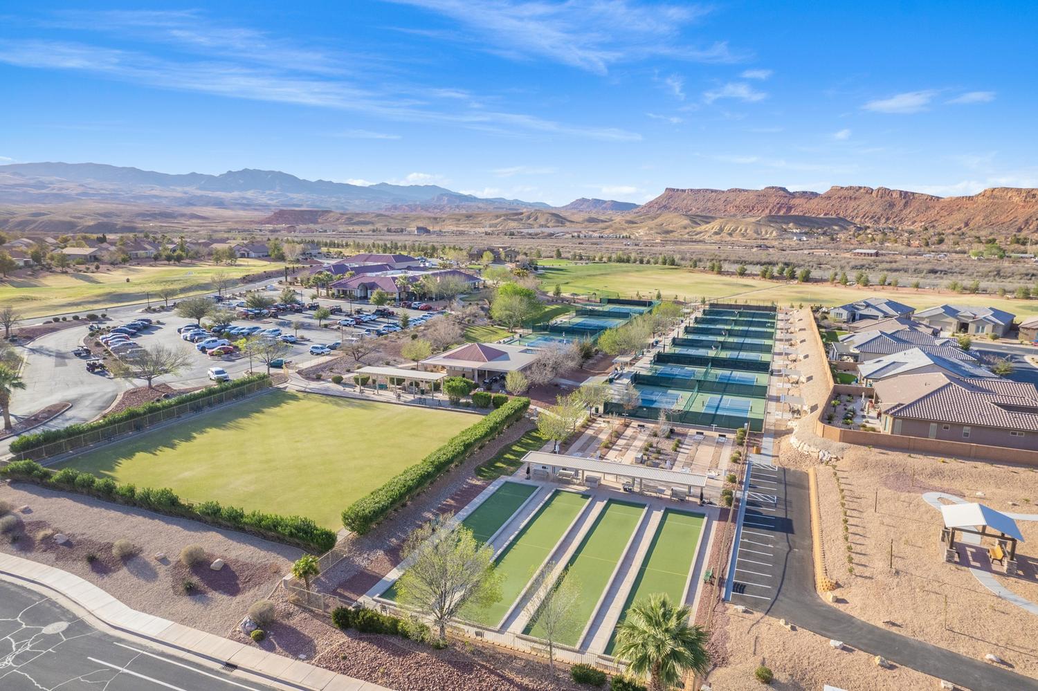 Expansive outdoor recreation area featuring multiple tennis courts, bocce ball courts, a large open lawn, covered seating areas, and architectural structures