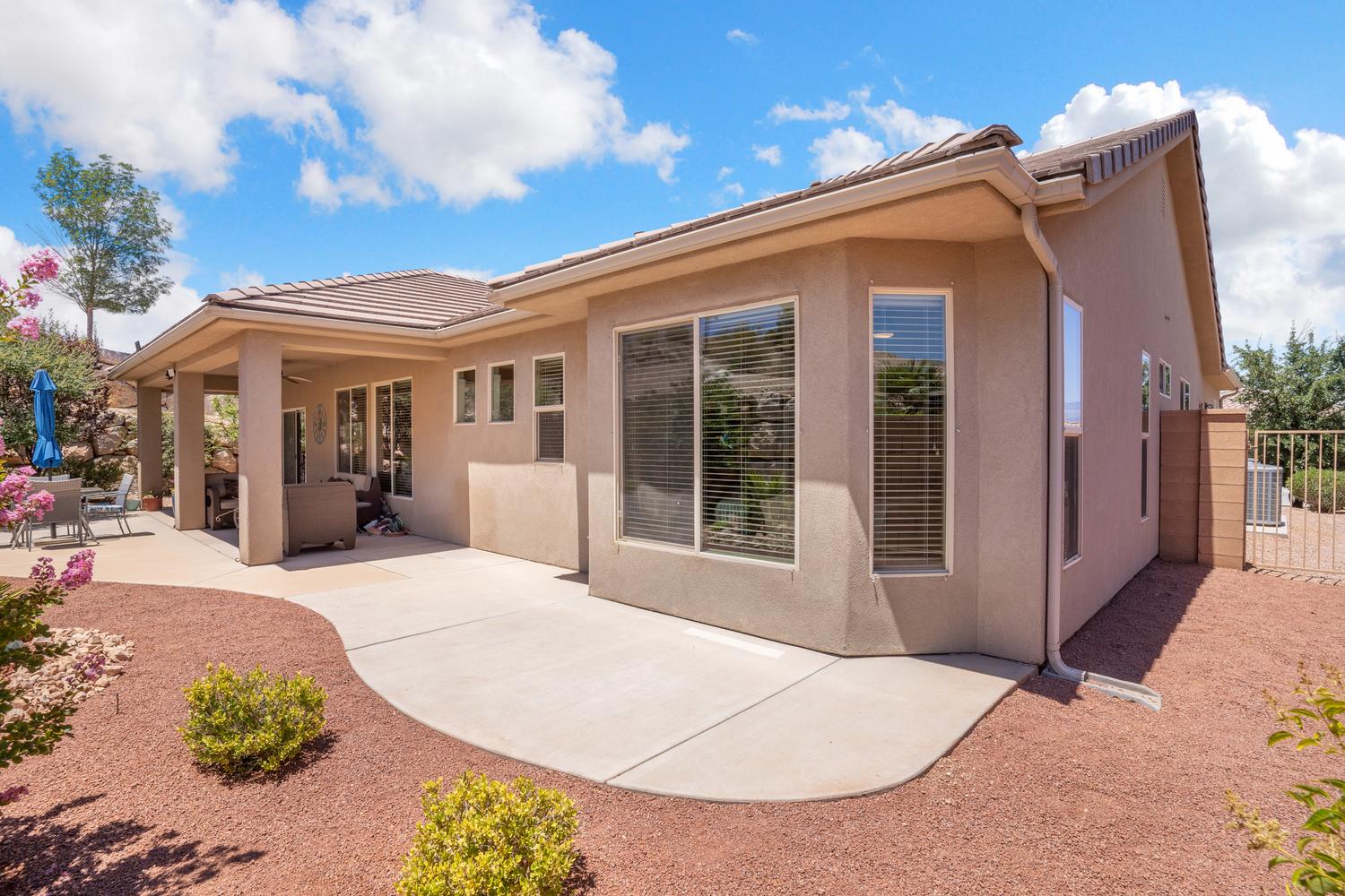 Exterior stucco finish with a covered patio, extensive concrete patio, and a low-maintenance landscape featuring crushed rock and plantings