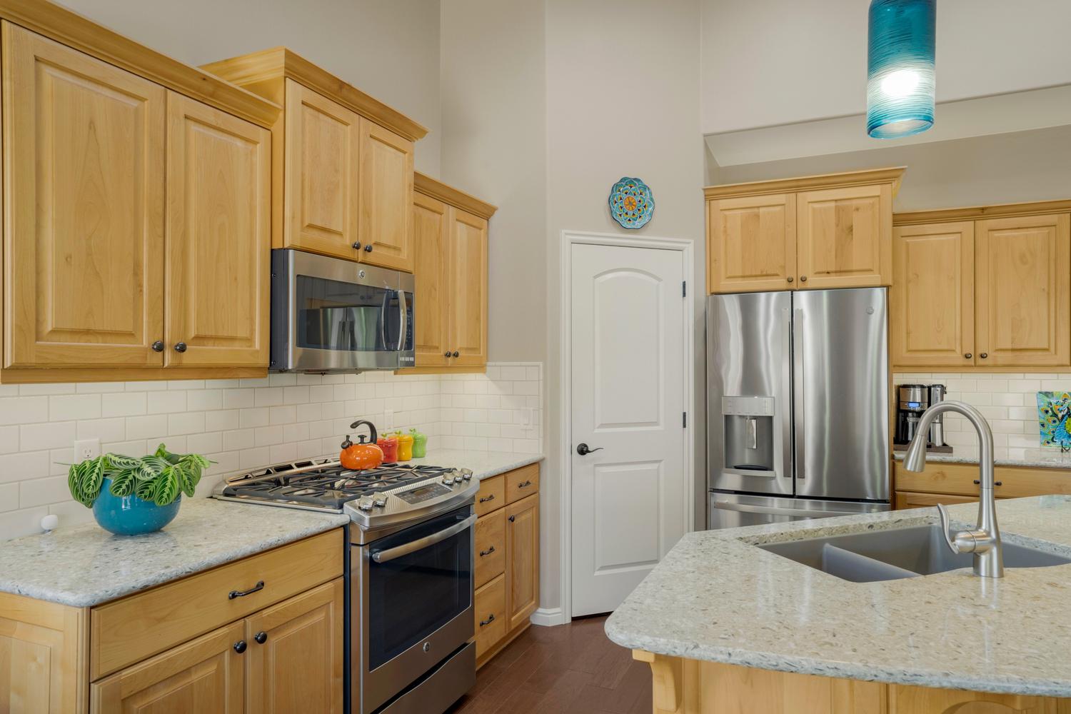 Kitchen featuring light wood cabinetry, stainless steel appliances, light speckled countertops, subway tile backsplash, and a double basin sink with a gooseneck faucet
