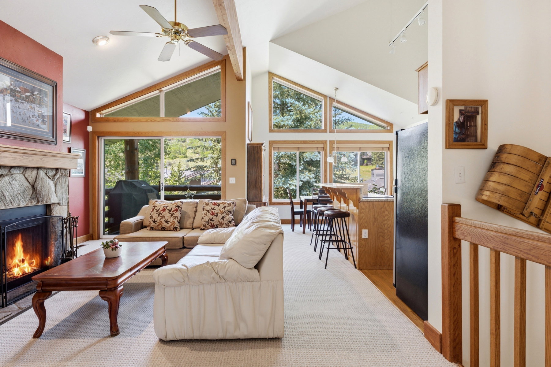Open concept living space featuring a stone-clad fireplace, vaulted ceilings with exposed wood beams, and a ceiling fan