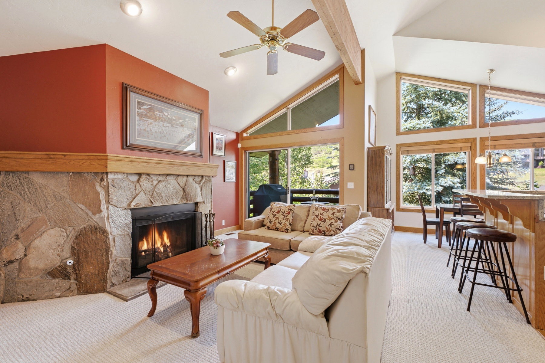 Living area featuring a stone-clad fireplace with wood mantel, vaulted ceilings with exposed beams, recessed lighting, and a ceiling fan