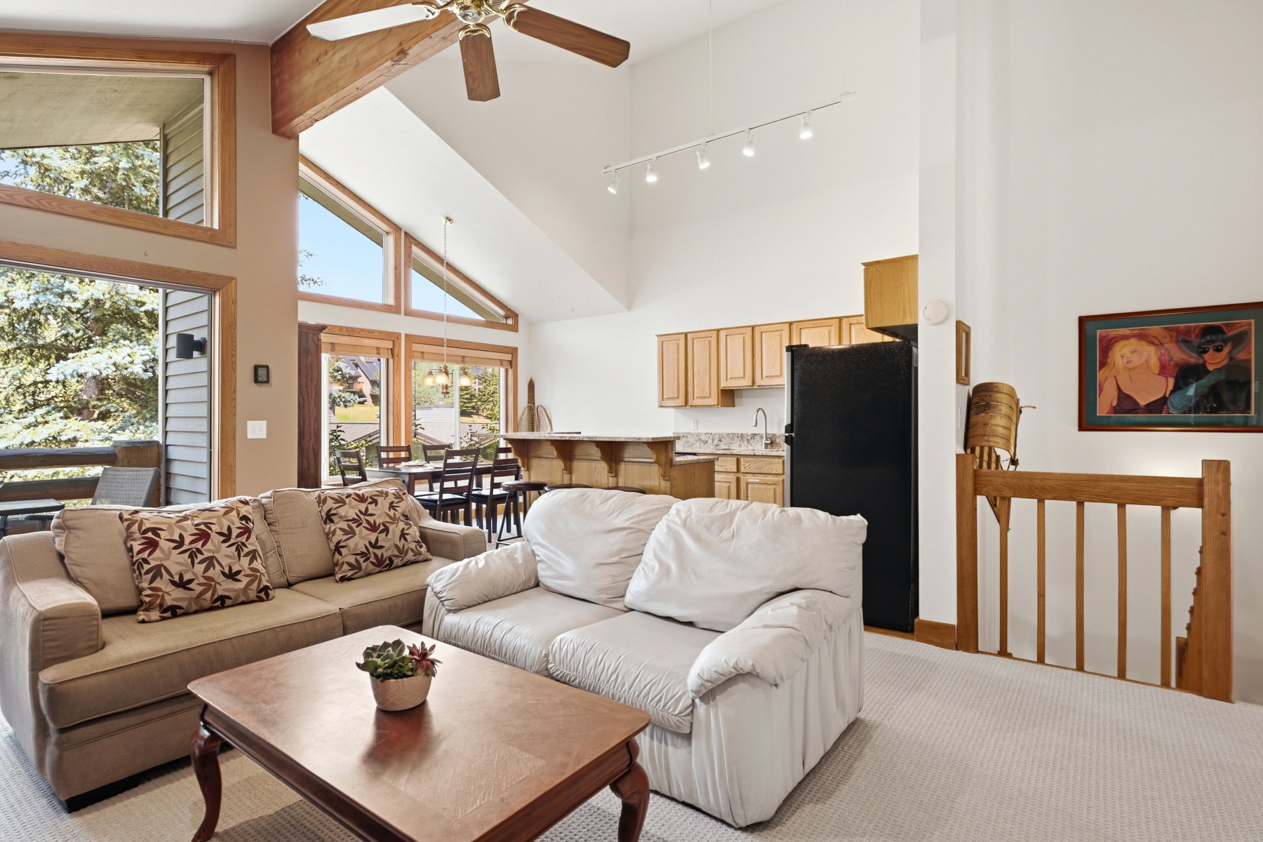 Spacious living area featuring vaulted ceilings with exposed wood beams, a ceiling fan, and track lighting
