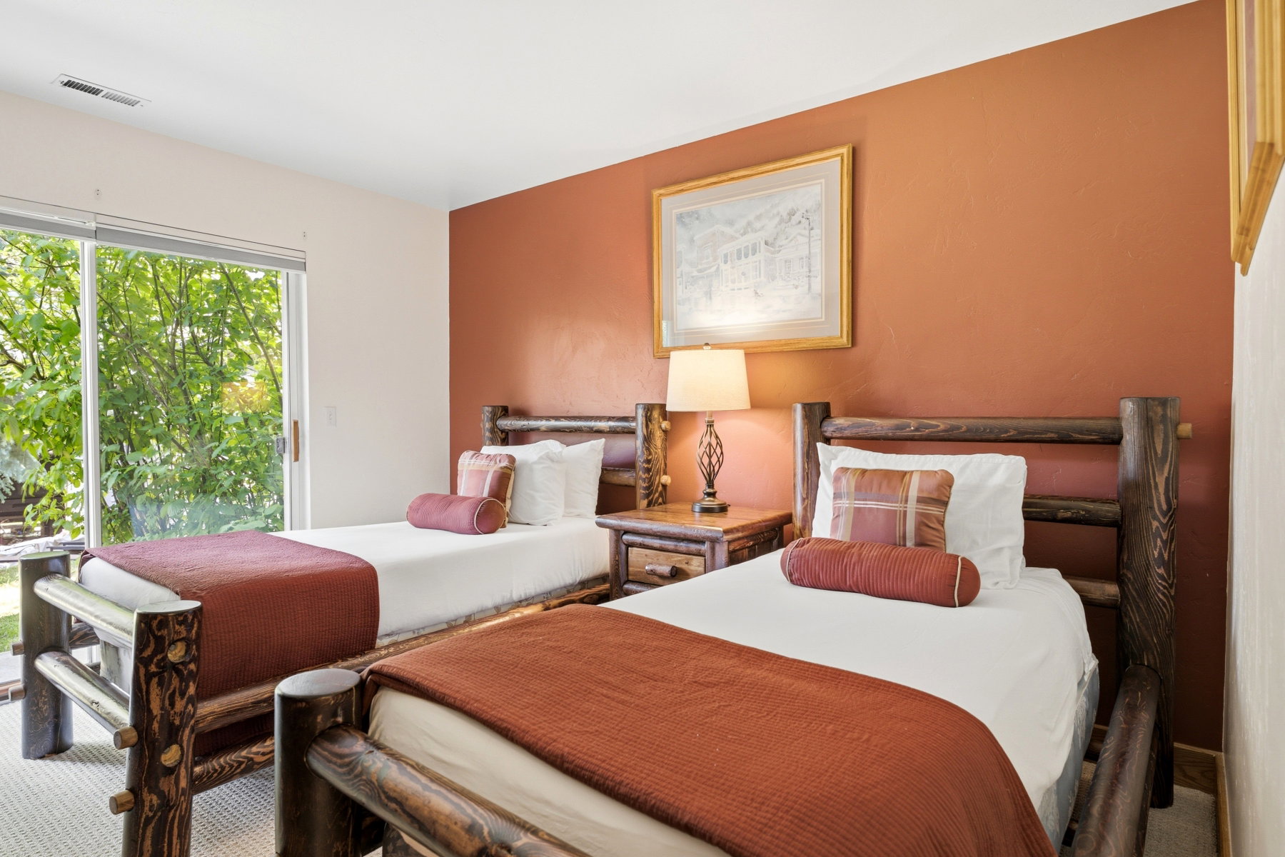 Warmly painted bedroom featuring two wood-frame beds, a wood nightstand, and a large sliding glass door