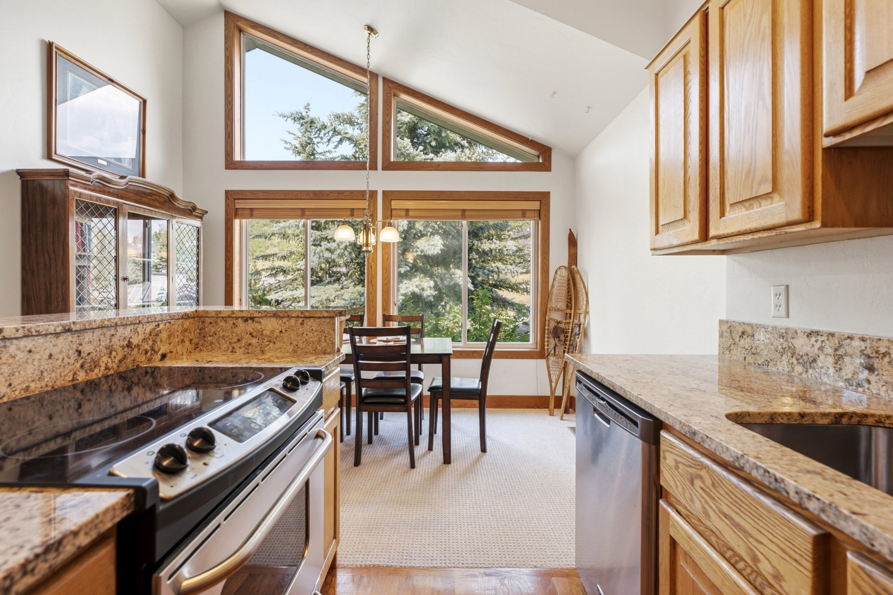Kitchen and dining area featuring vaulted ceilings with natural wood window frames, light-toned cabinetry, granite countertops, and stainless steel appliances