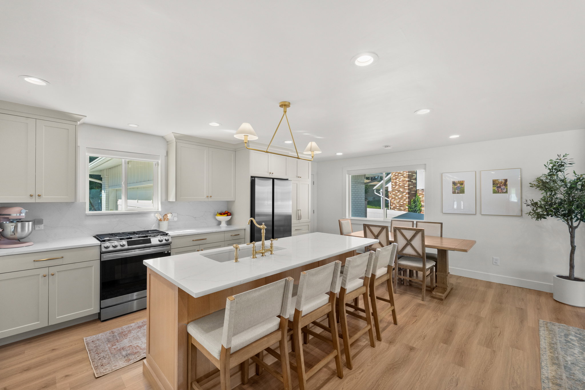 Open-concept kitchen featuring light wood-finish flooring, white cabinetry with gold hardware, a large central island with seating, a stainless steel range, and a dining area