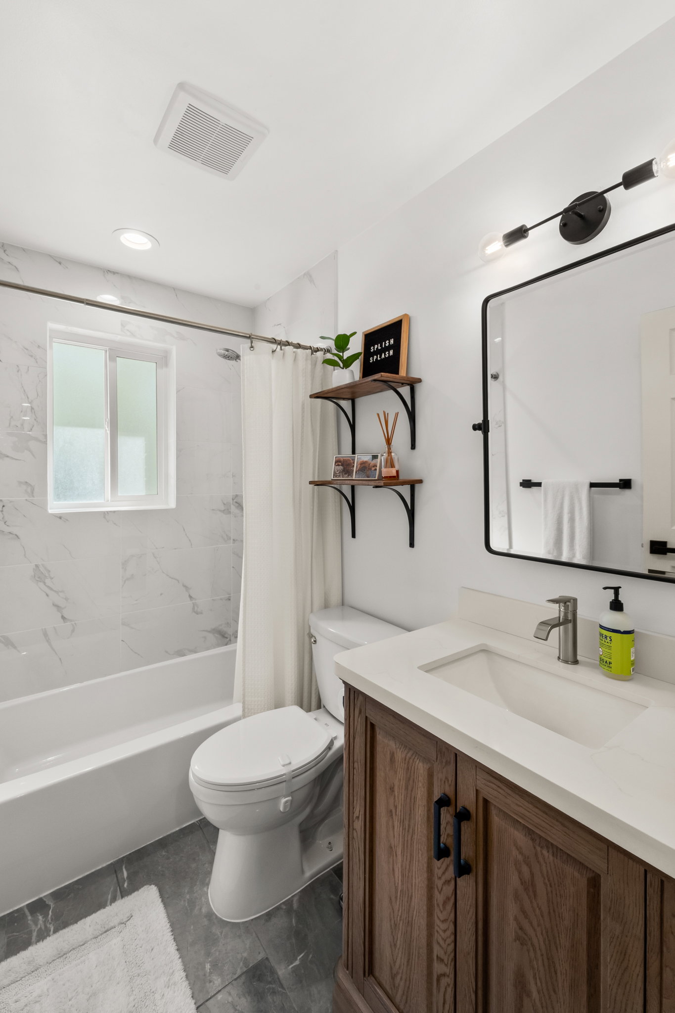 Full bathroom with a white bathtub and shower featuring white and gray marble-look tile