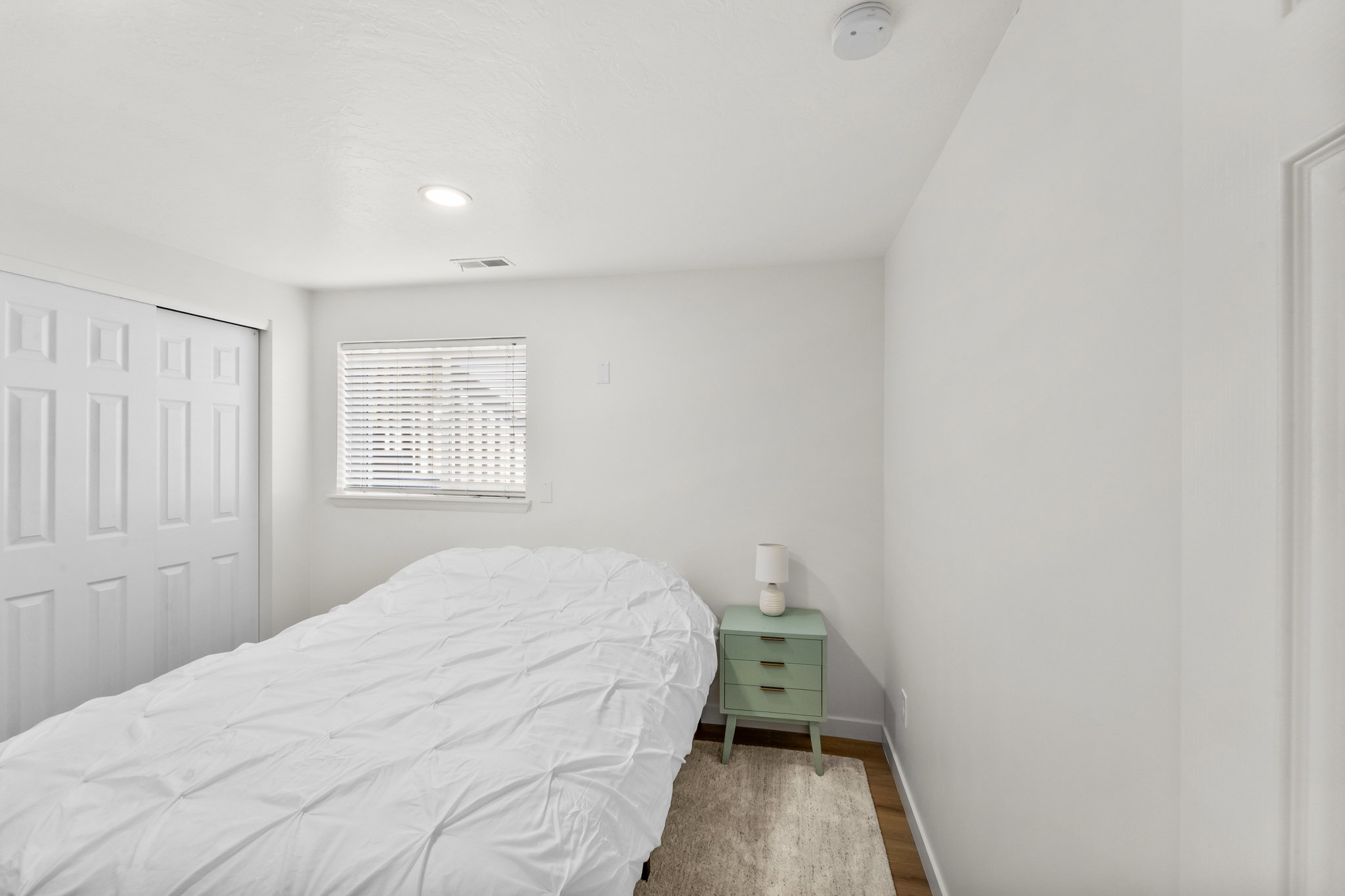 Bright interior space featuring a window with horizontal blinds, recessed lighting, and wood-finish flooring
