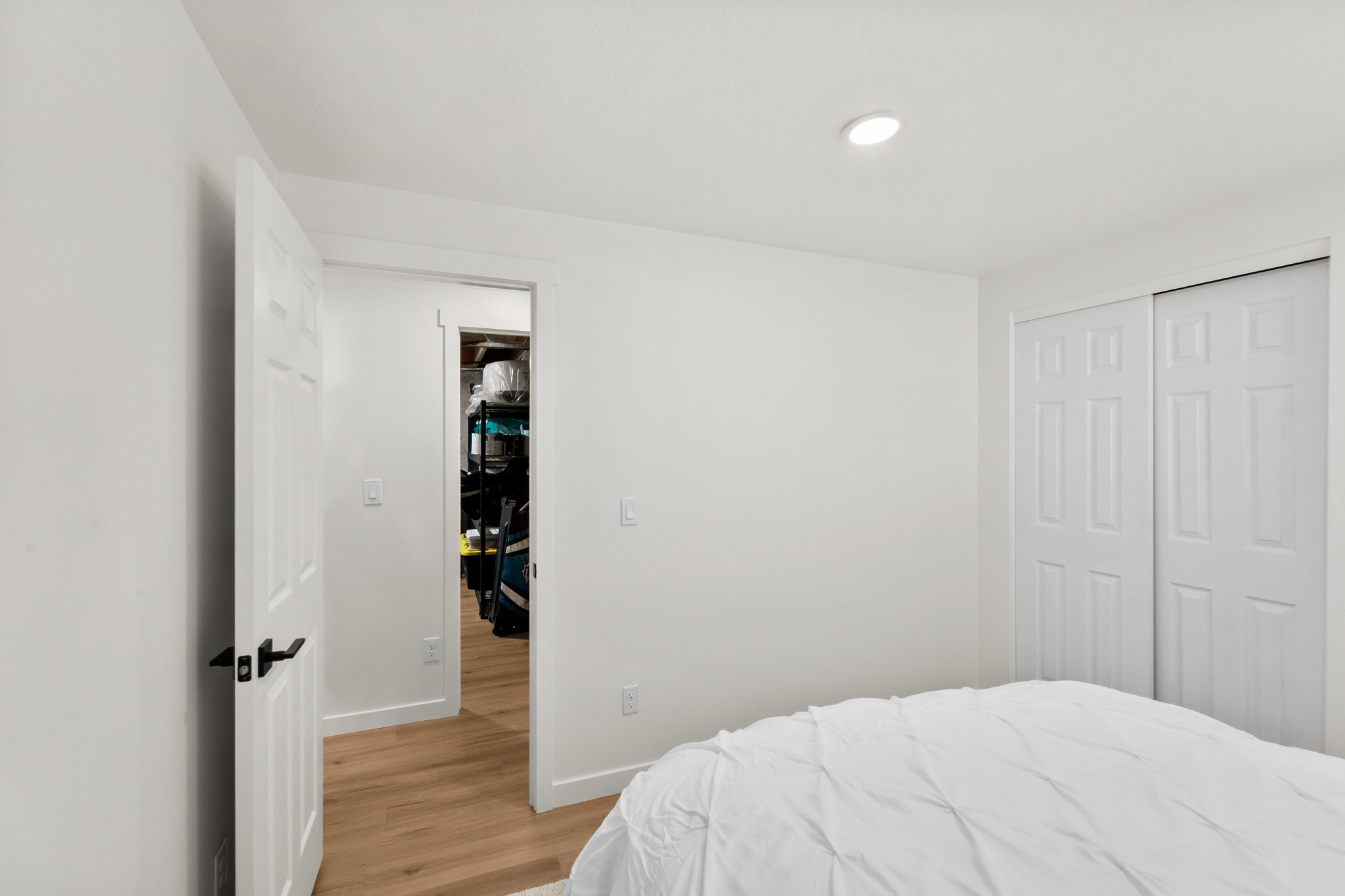 White interior with recessed lighting, wood-finish flooring, a paneled door with black hardware, and a bifold closet door