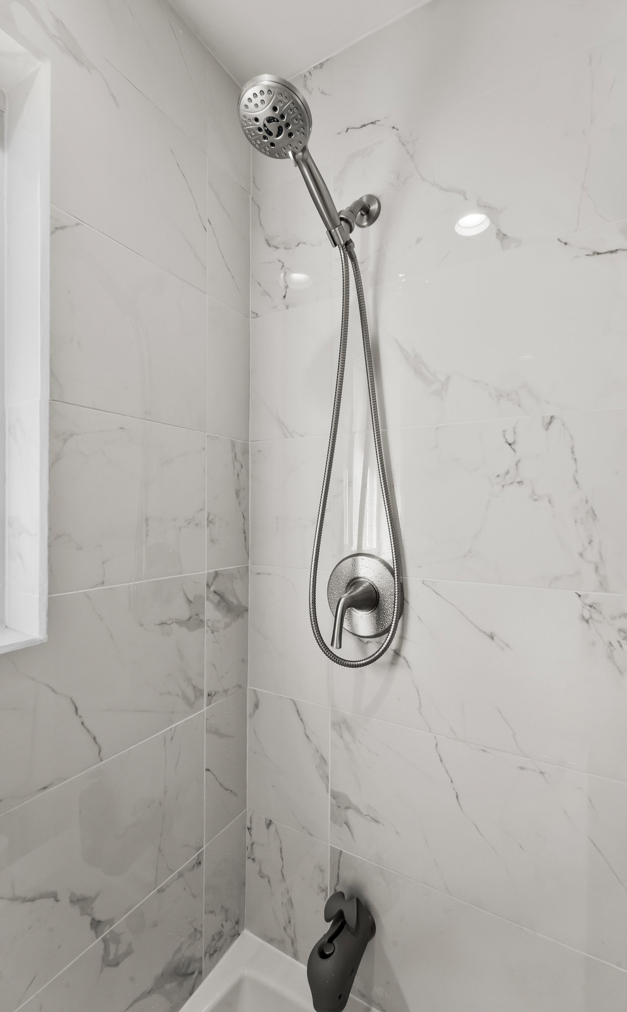 Contemporary shower with a handheld showerhead, single-handle control, and white marble-look wall tiling