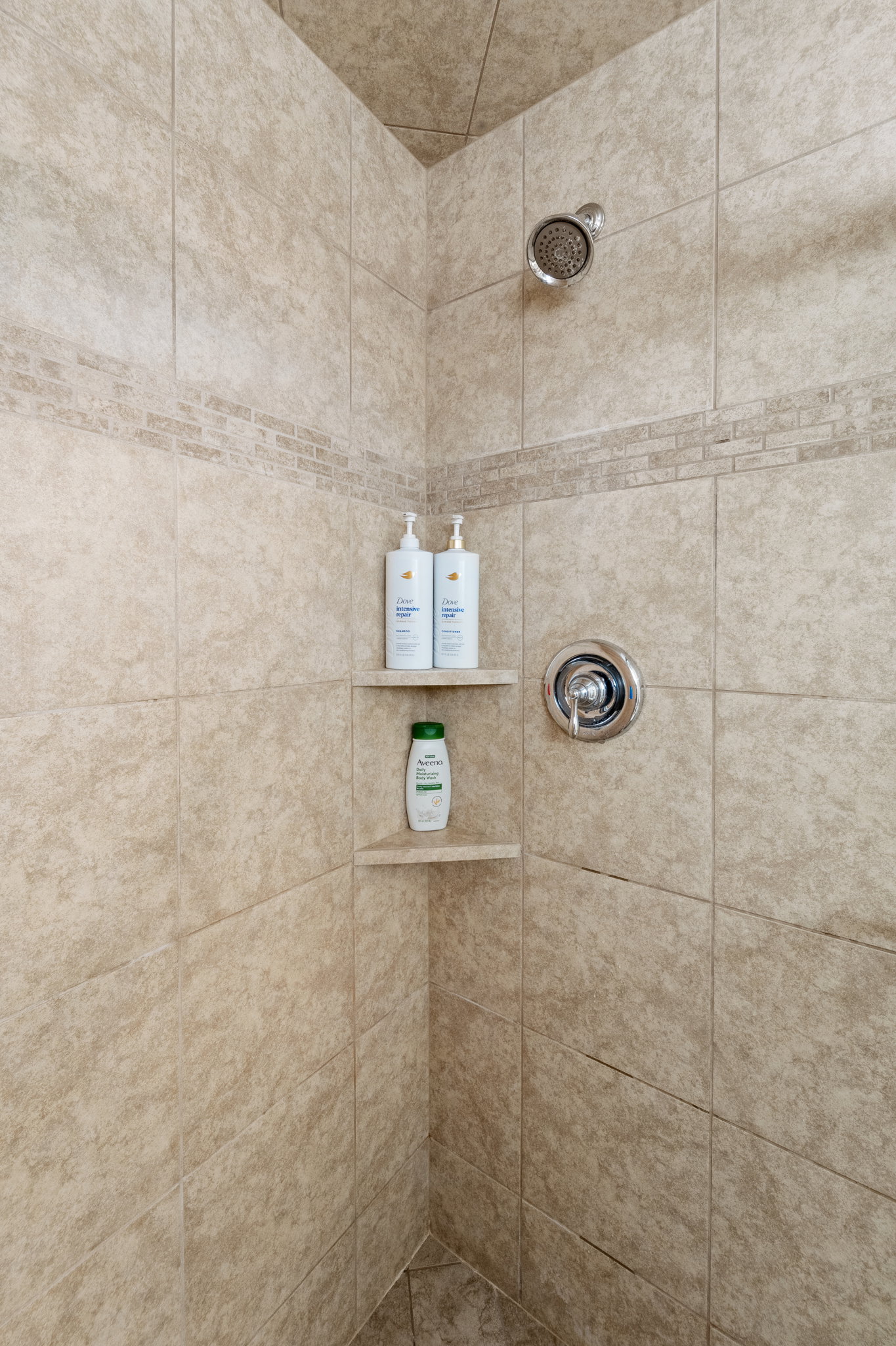 Tiled shower enclosure featuring a mosaic accent band, built-in corner shelving, and chrome fixtures