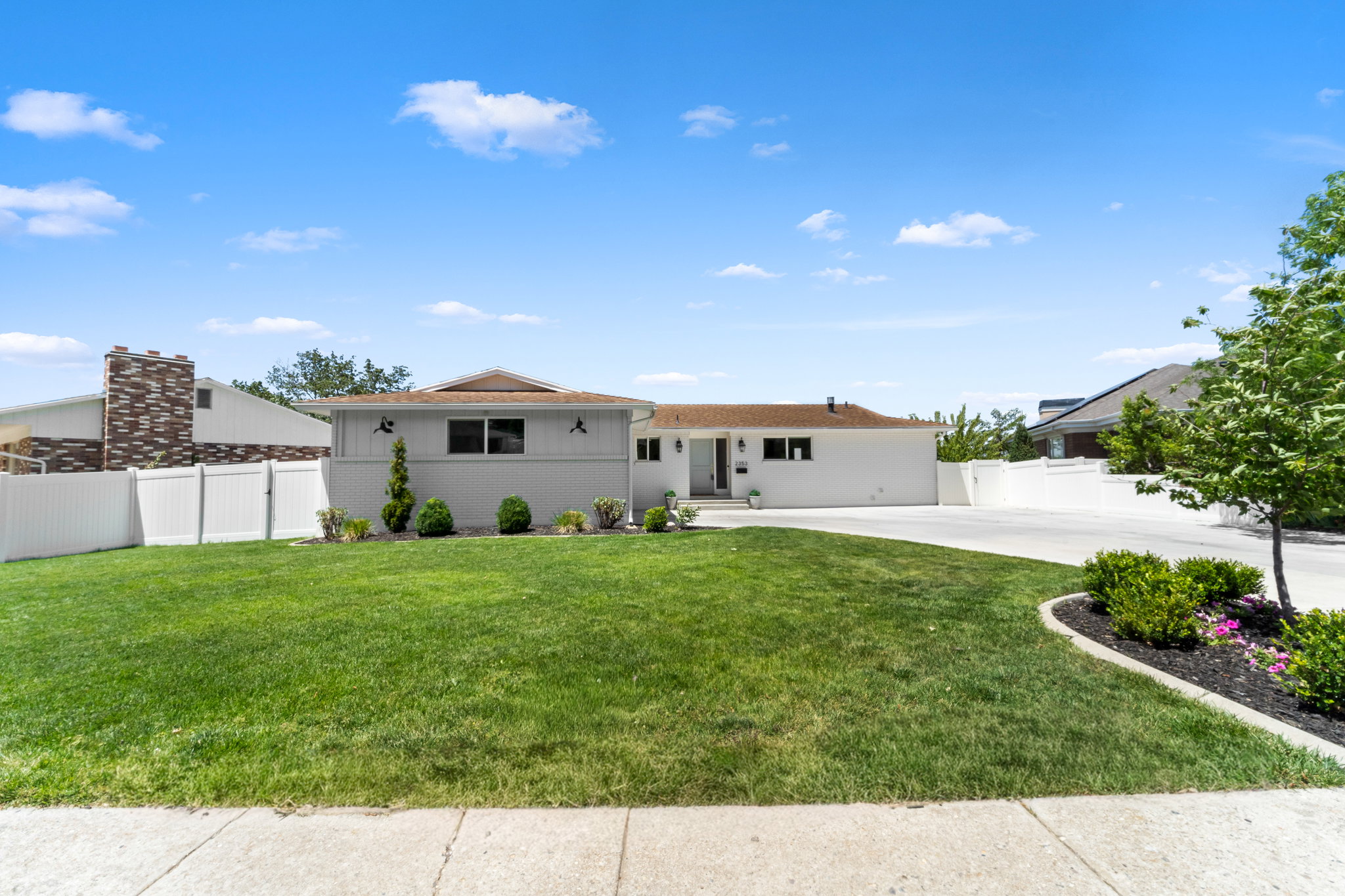 Expansive front lawn with mature landscaping and concrete driveway
