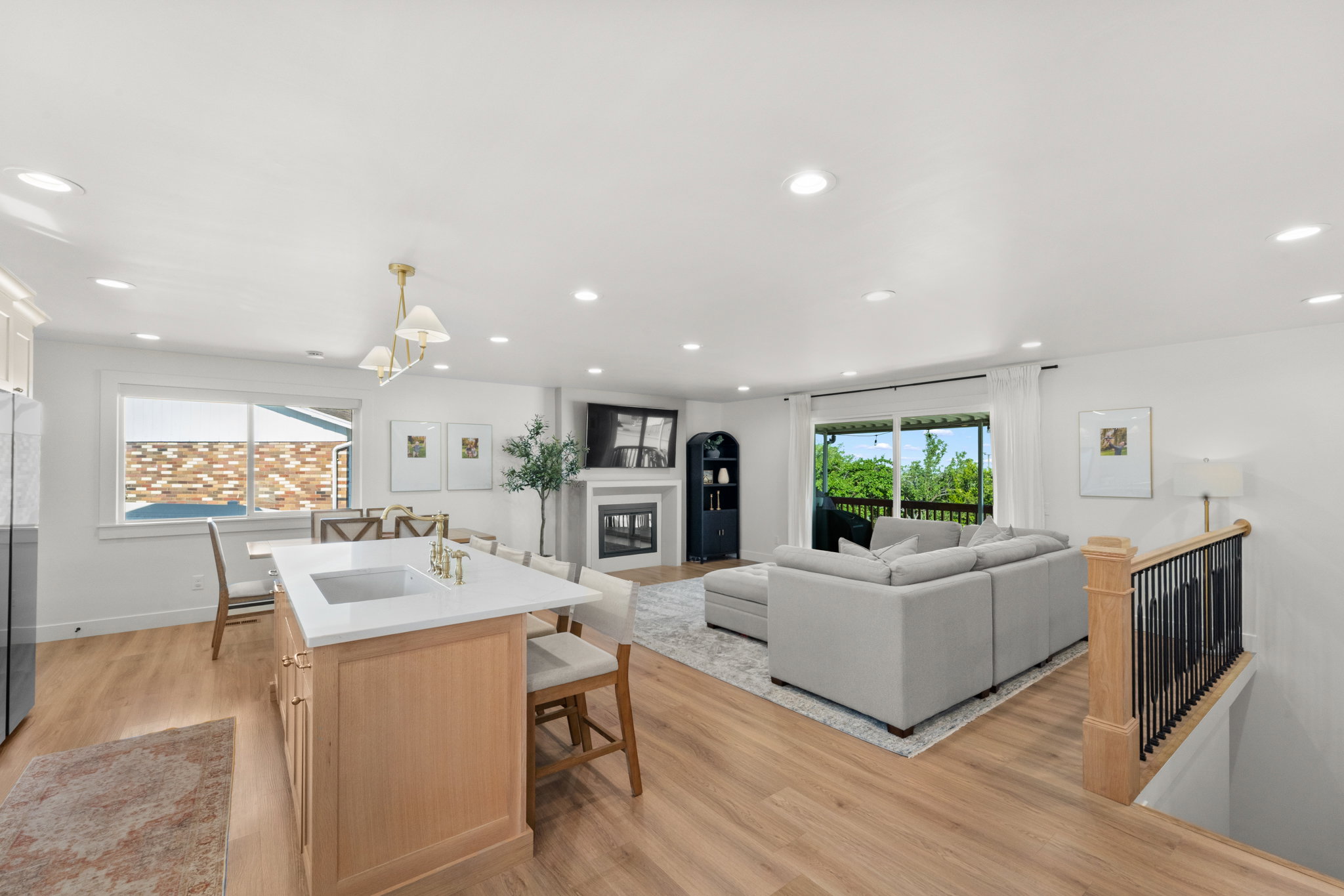 Open-concept living area featuring wood-finish flooring, recessed lighting, and a kitchen island with a built-in sink and gold-tone faucet