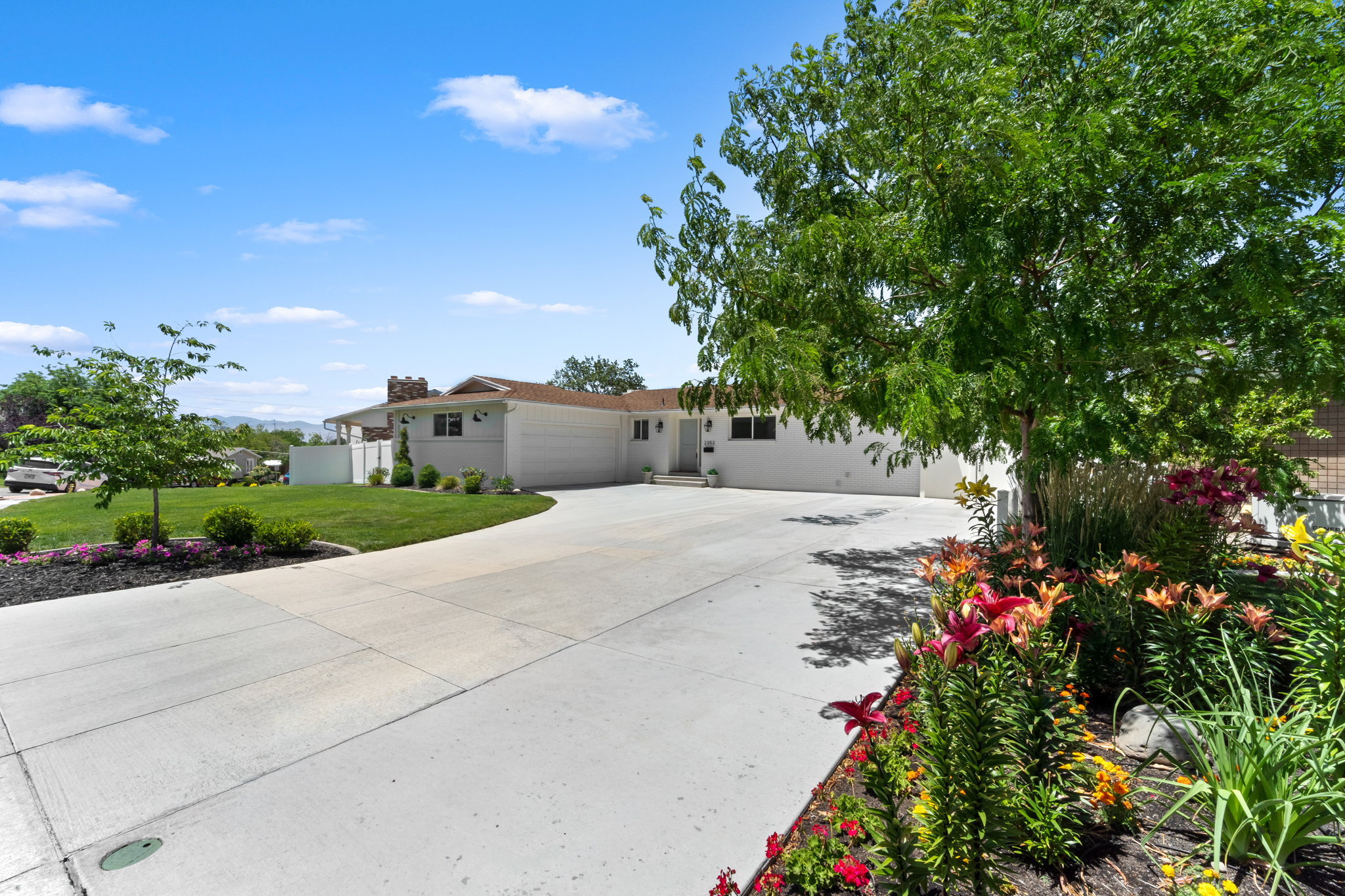 Spacious concrete driveway leading to a residence featuring a white exterior, attached garage, and a lush green lawn