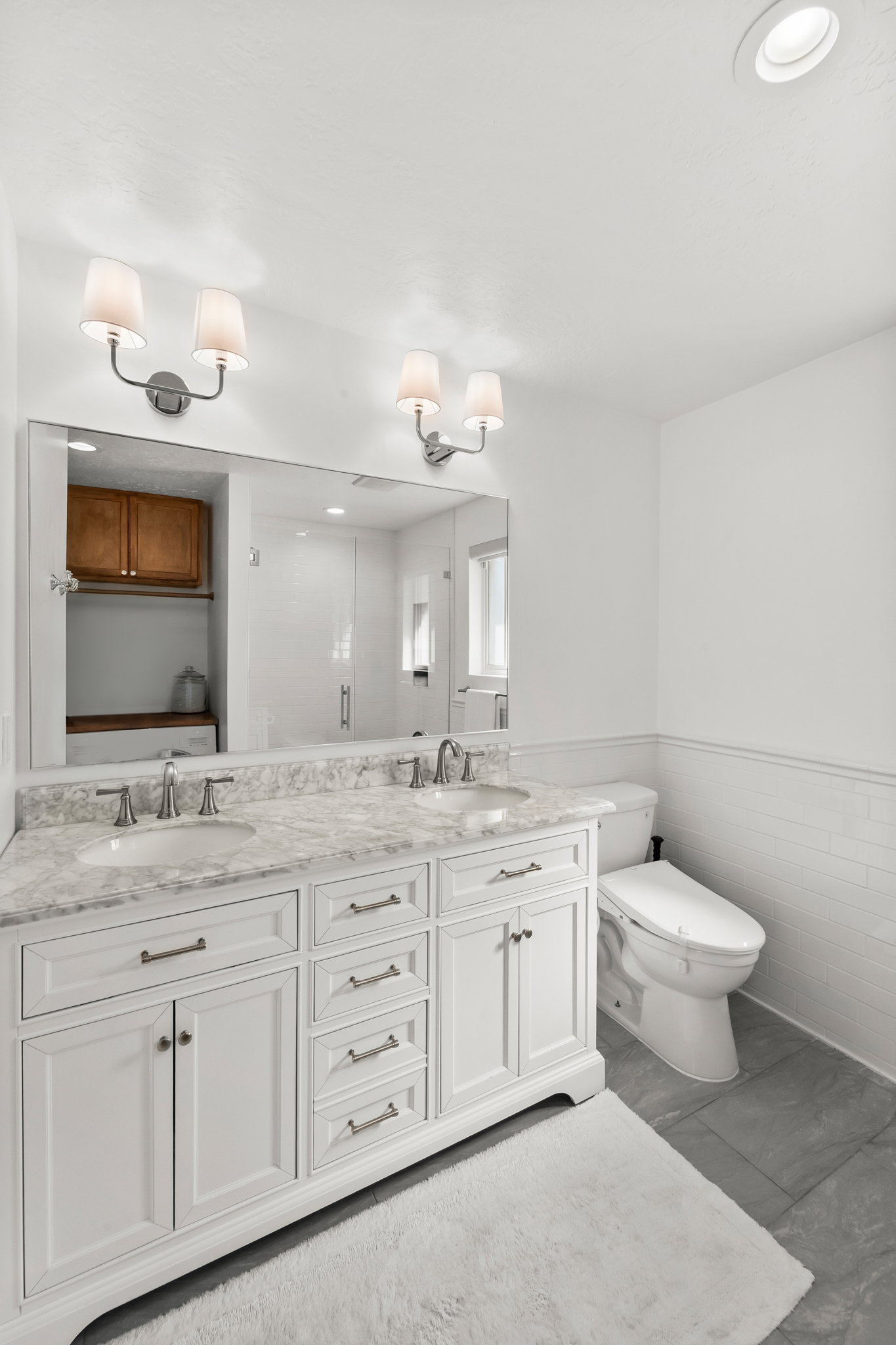 Spacious bathroom featuring a dual vanity with a stone-finish countertop, white cabinetry, and brushed nickel hardware