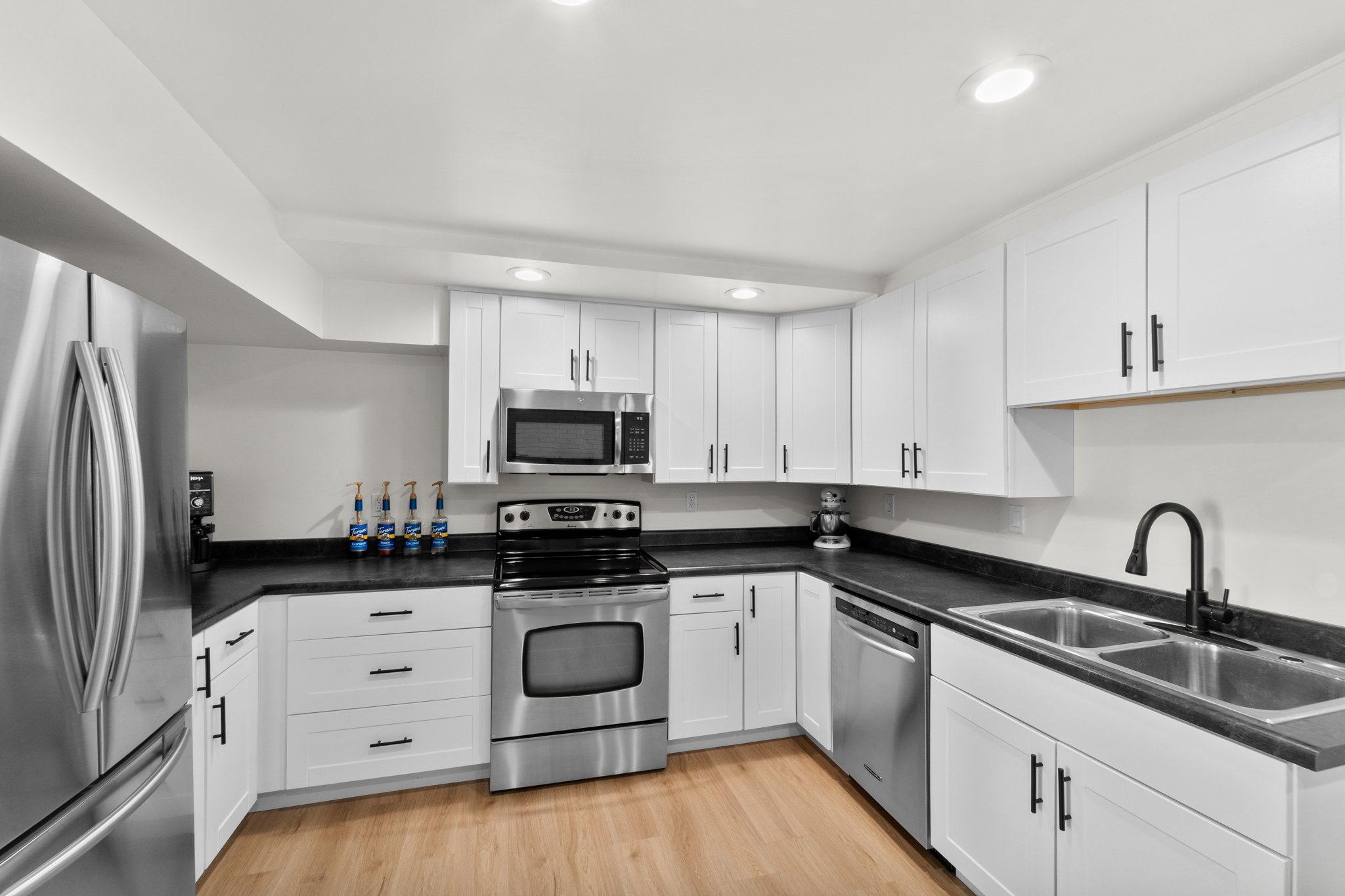 Modern kitchen featuring white shaker cabinetry, stainless steel appliances, dark countertops, and wood-finish flooring