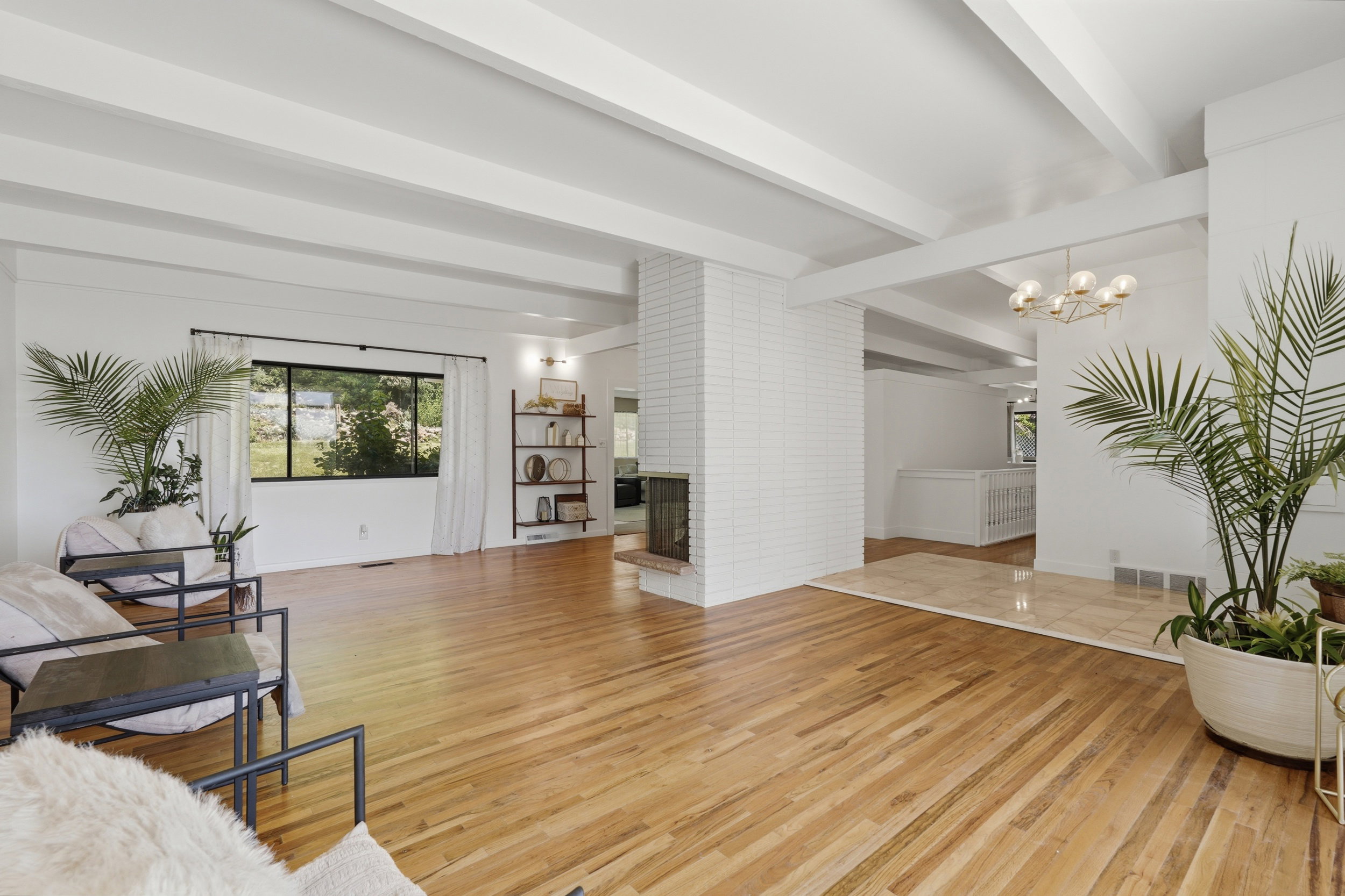 Expansive room featuring wood-finish flooring, exposed ceiling beams, and a white brick fireplace