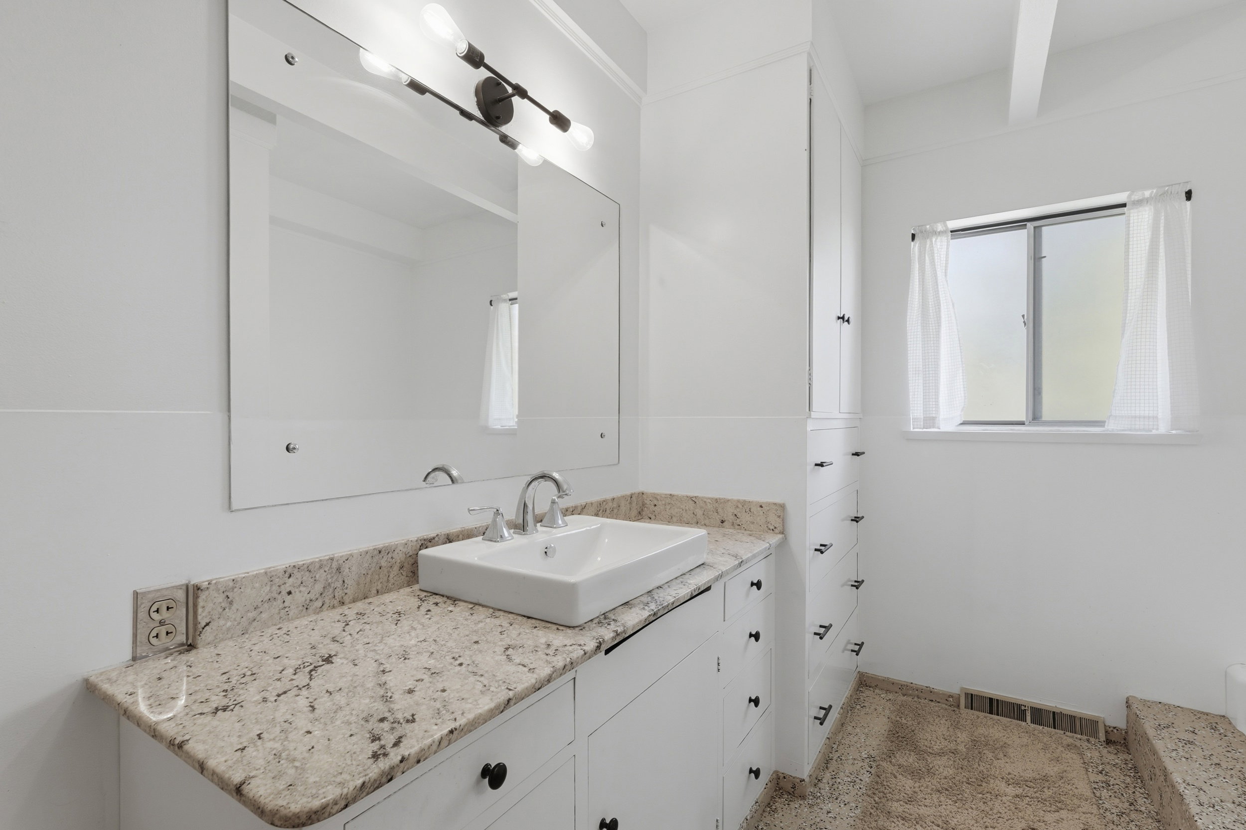 Level 1 bathroom featuring a vessel sink, stone countertop, built-in storage cabinetry, and a window with privacy glass
