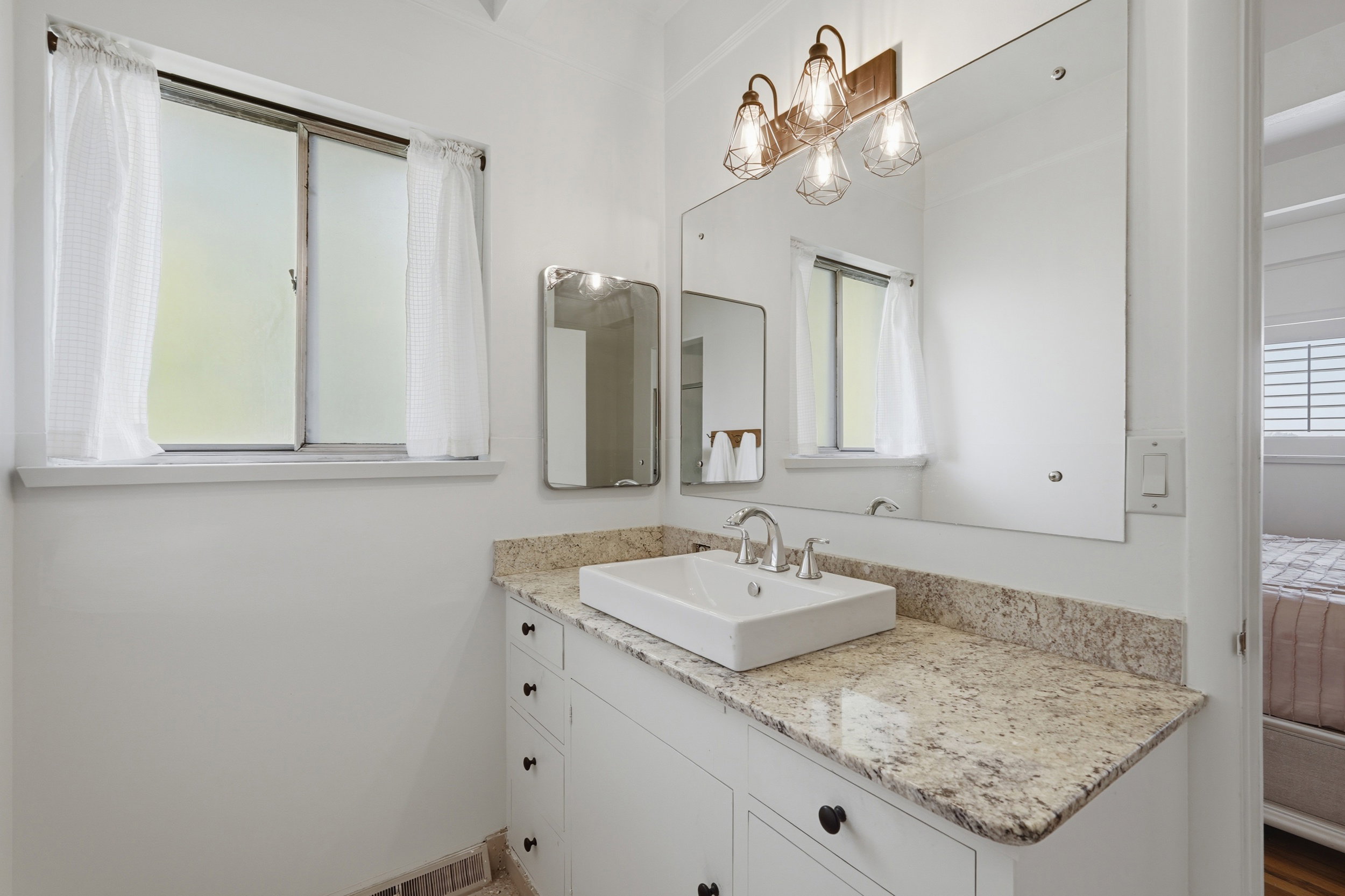 Primary bathroom vanity with a rectangular vessel sink, stone countertop, and white cabinetry featuring black hardware