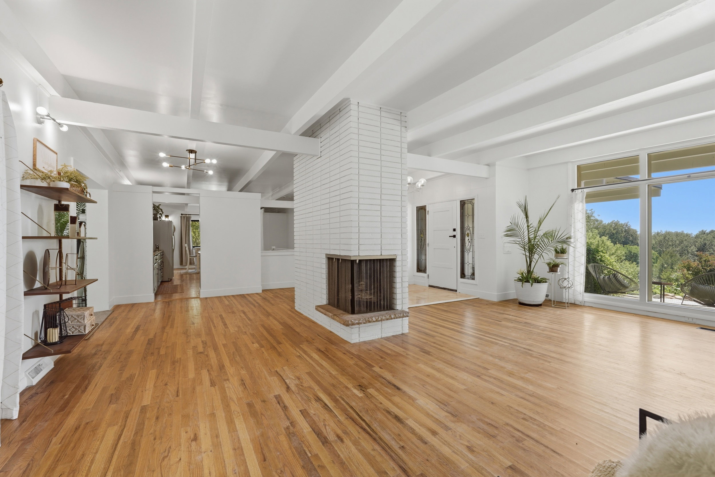 Spacious living area featuring exposed beam ceilings, wood-finish flooring, a white brick fireplace, and large sliding glass doors providing outdoor access