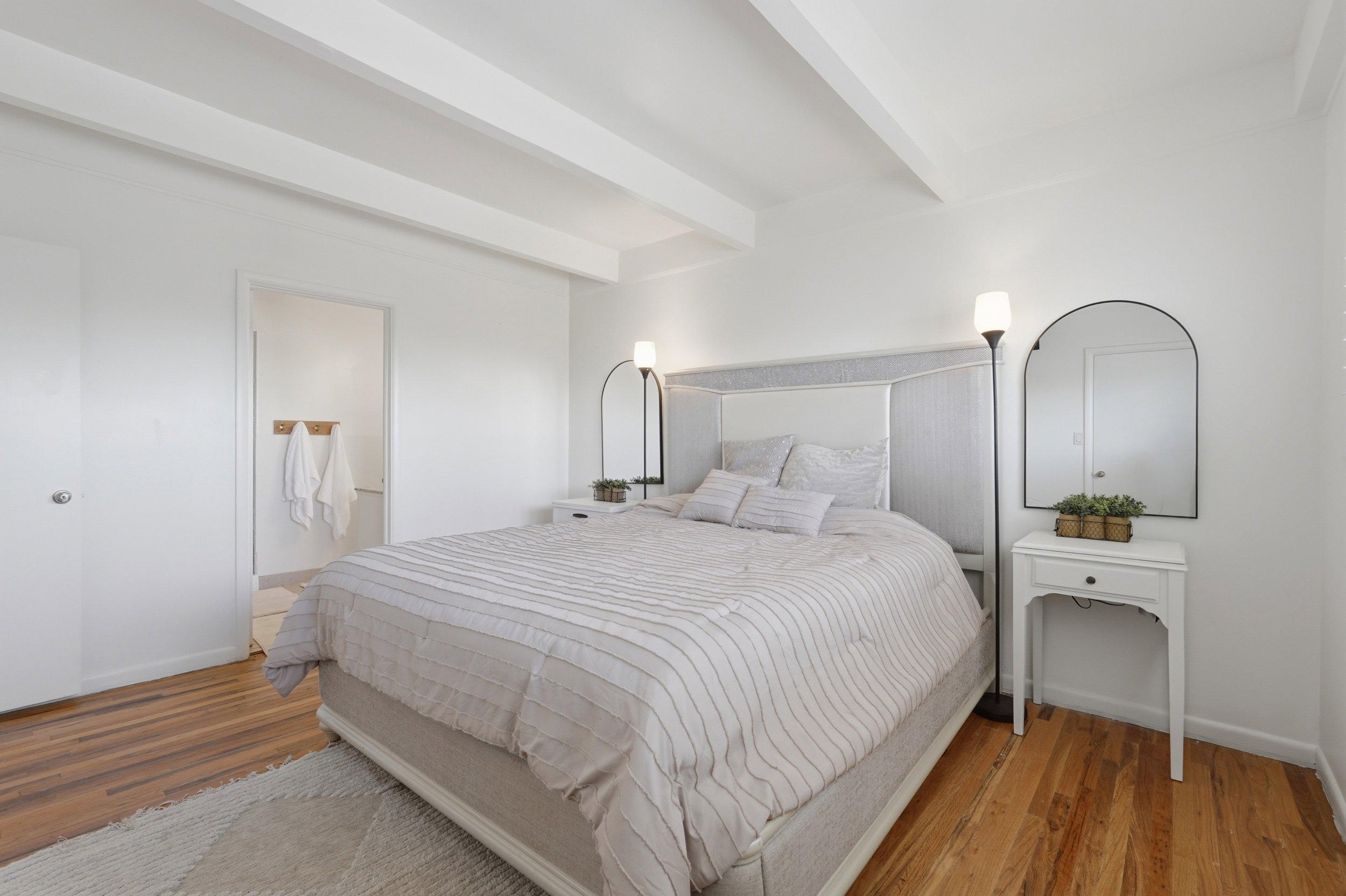 Primary bedroom featuring exposed ceiling beams, wood-finish flooring, and a white paneled door