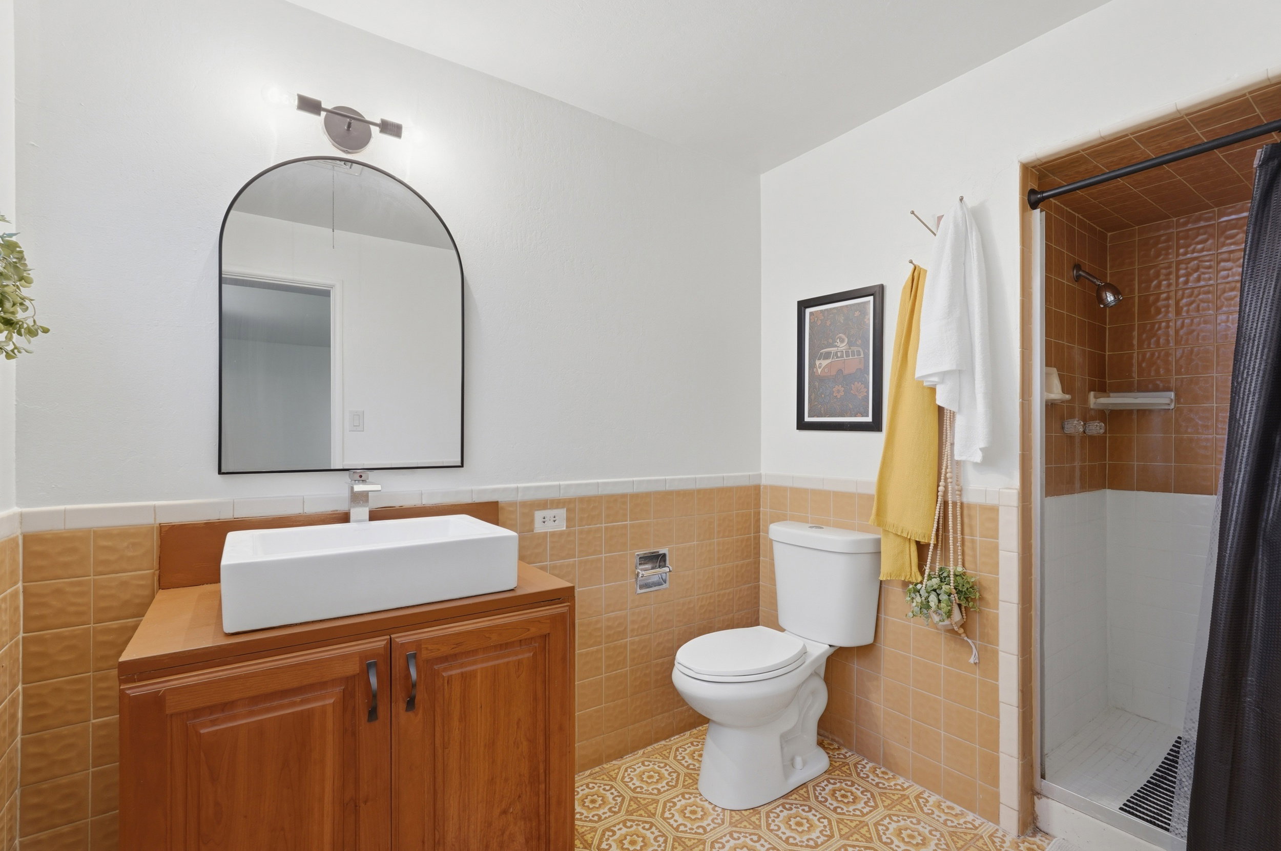 Bathroom featuring a vanity with a white vessel sink, a large arched mirror, and a shower with tiled walls
