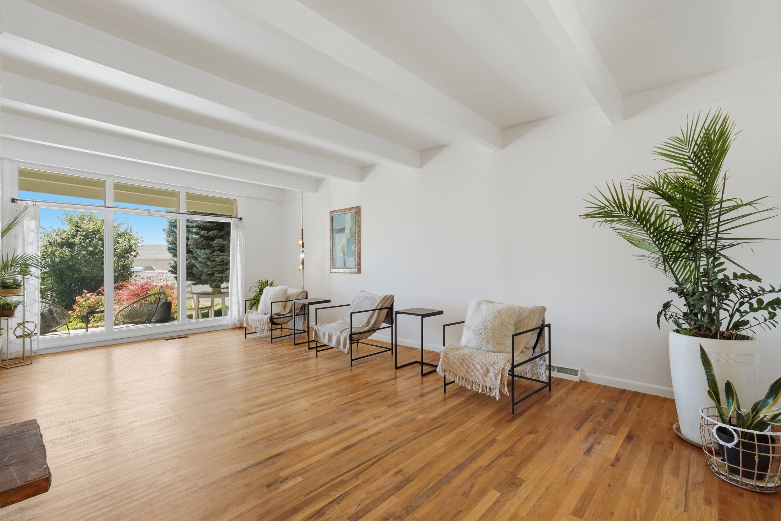 Spacious living area featuring large windows, wood-finish flooring, white exposed beam ceiling, and white wall finishes