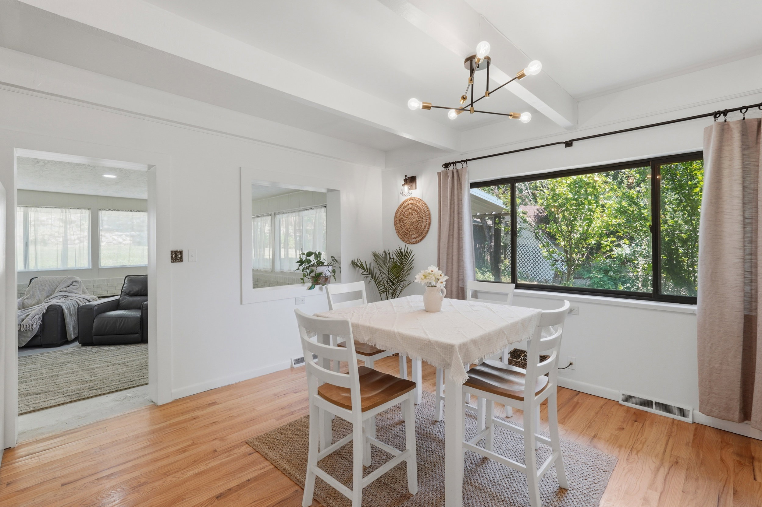 Dining area featuring wood-finish flooring, a contemporary ceiling light fixture, and a large window with exterior landscaping beyond