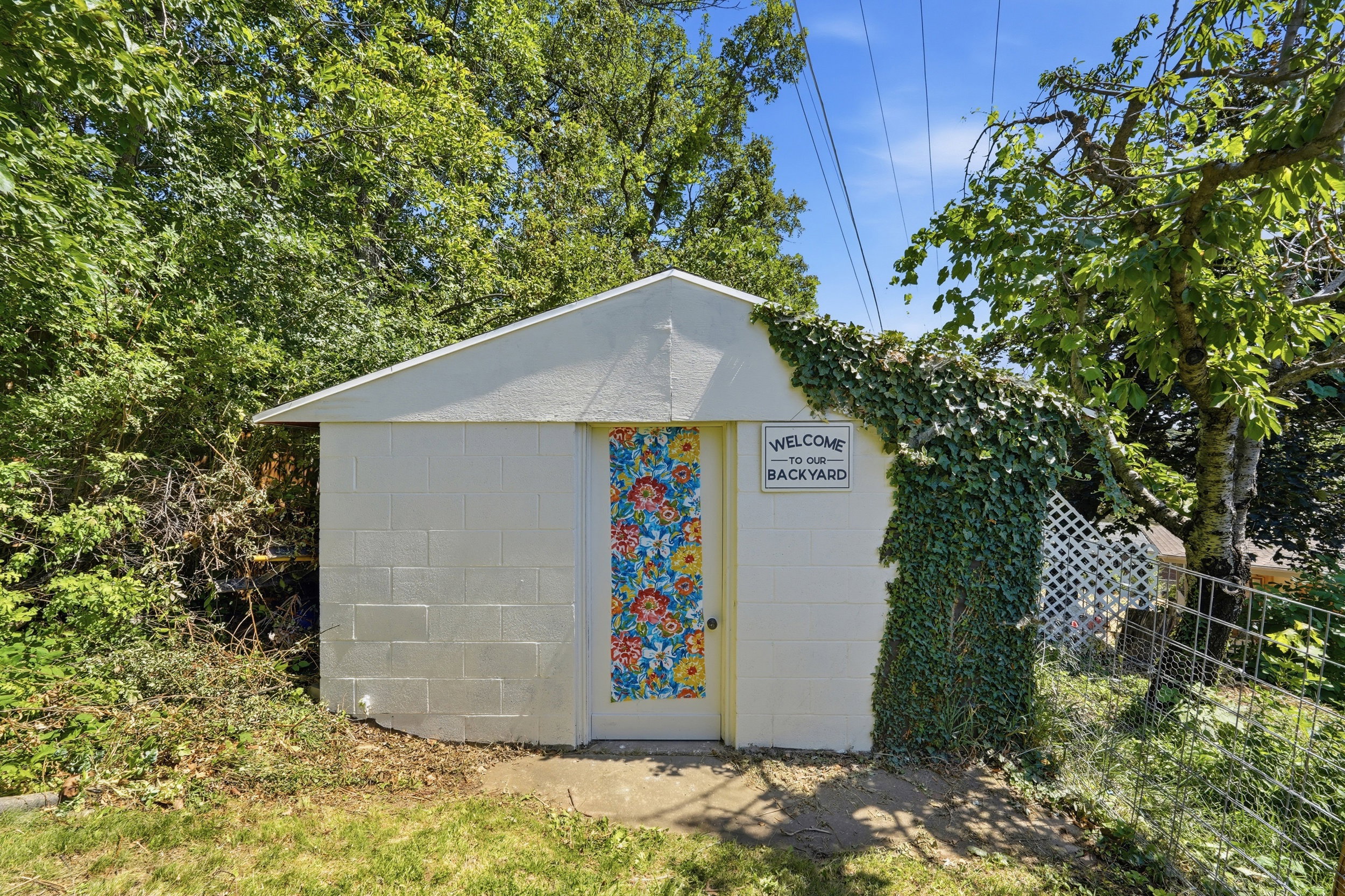 Freestanding utility building featuring a gable roof, painted block wall construction, and a vibrant floral-patterned door