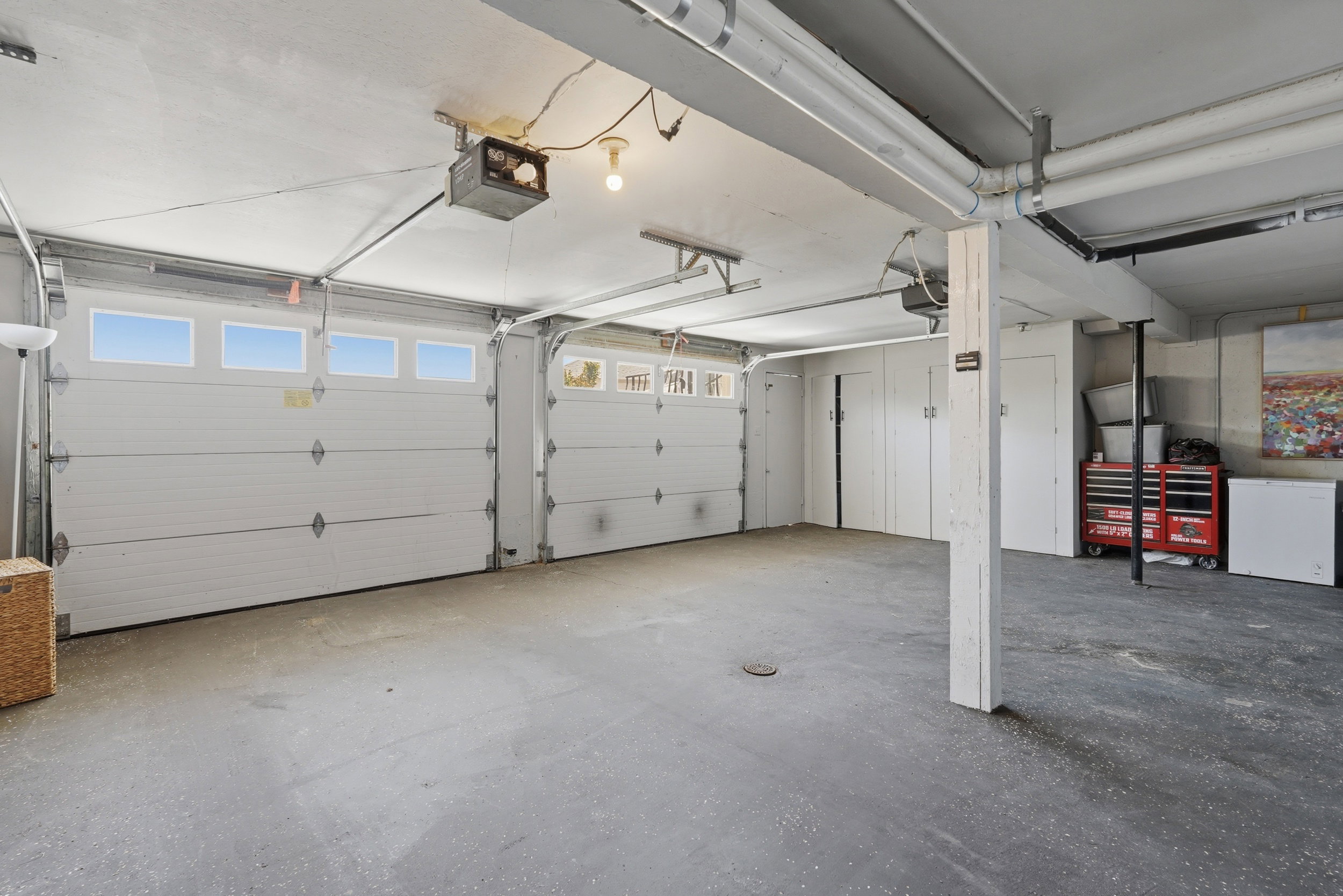 Spacious garage featuring two overhead doors with upper window panels, concrete flooring, exposed ceiling beams, and built-in storage cabinetry
