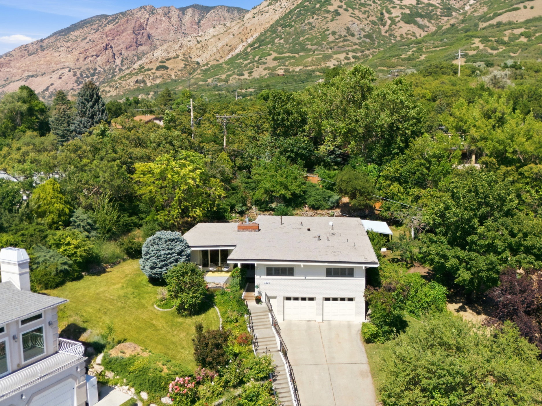 Contemporary residence featuring a two-car garage, mature landscaping, and a sloped driveway
