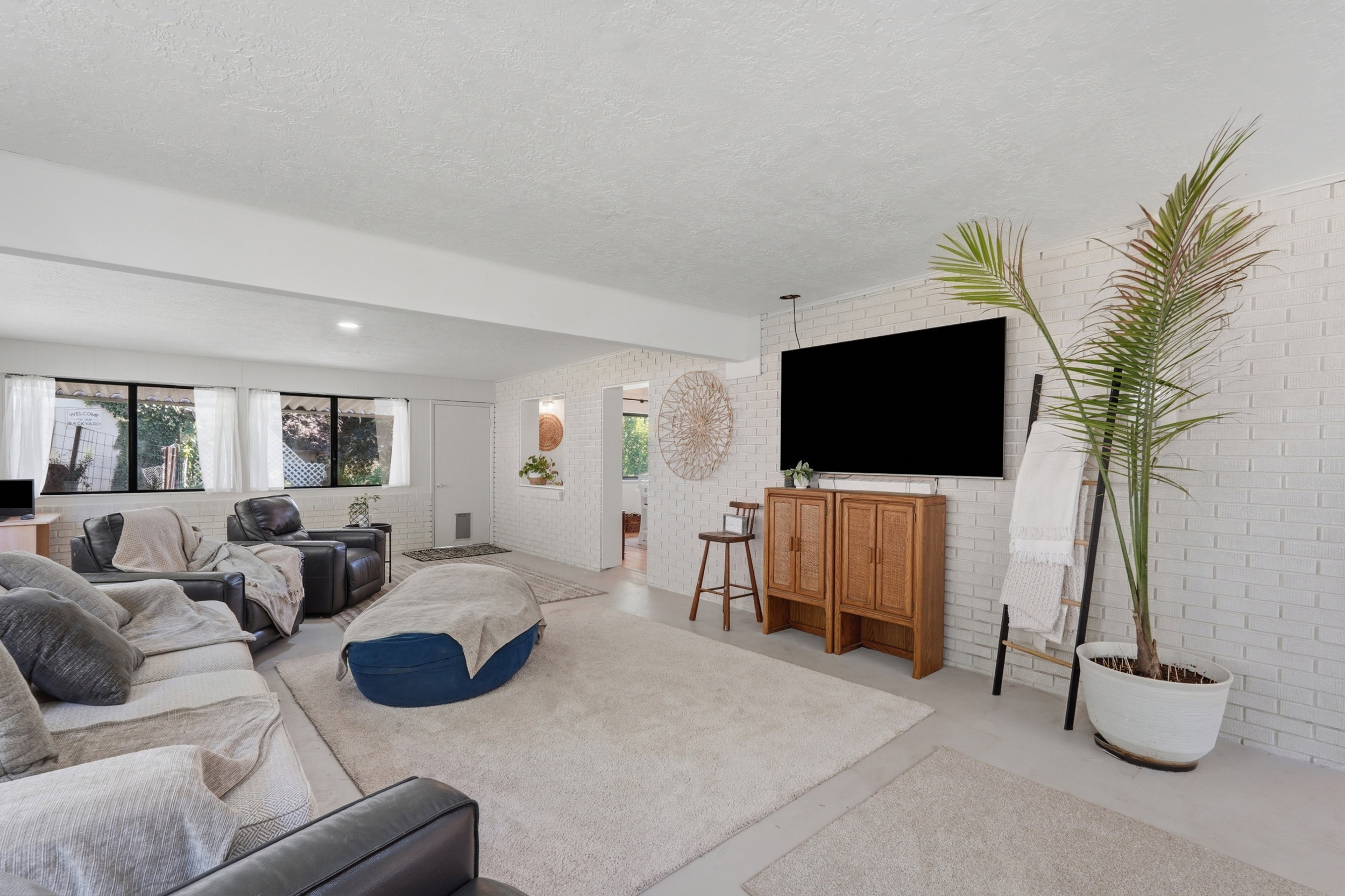 Spacious living area featuring white painted brick walls, recessed lighting, multiple windows, and light-toned flooring