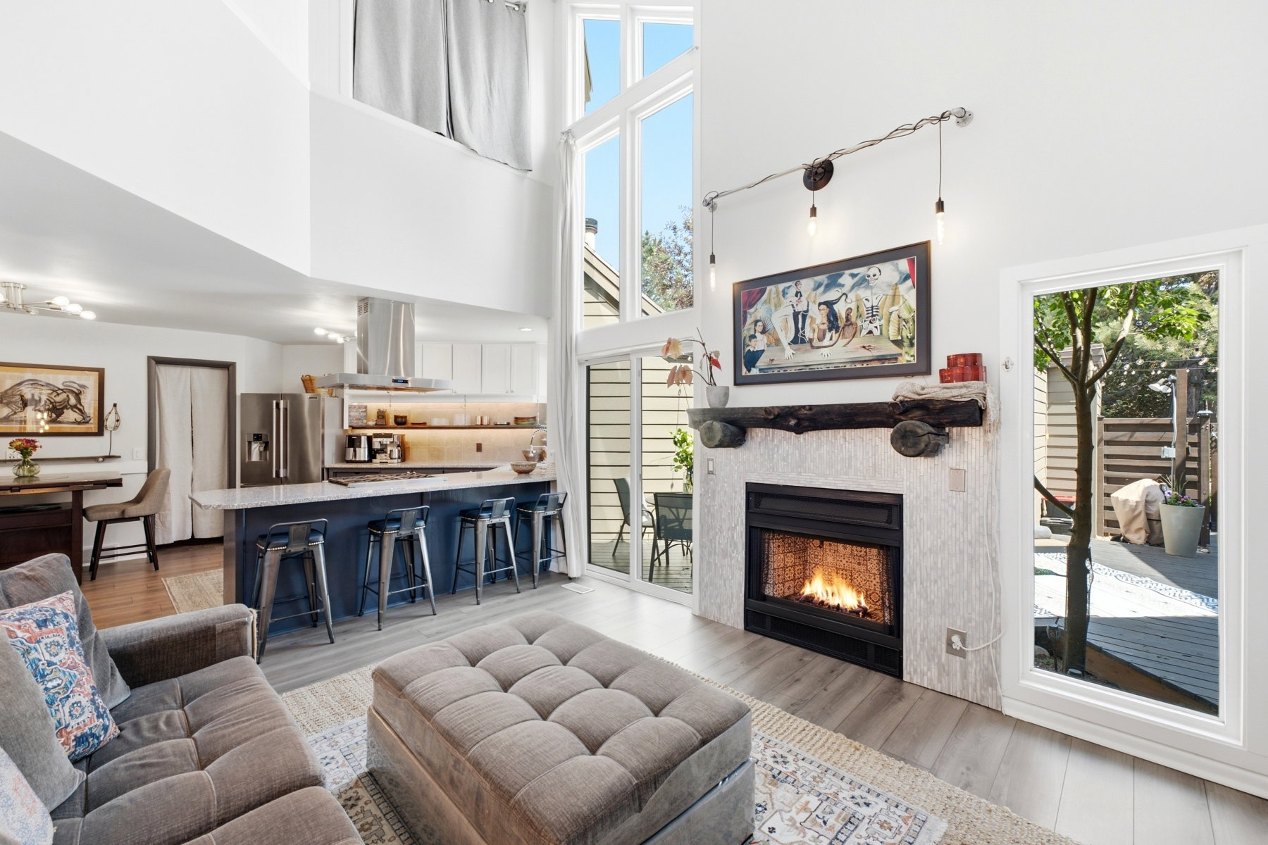 Vaulted ceiling living area featuring a fireplace with a wood mantle, a kitchen with an island, and a sliding glass door to an outdoor deck