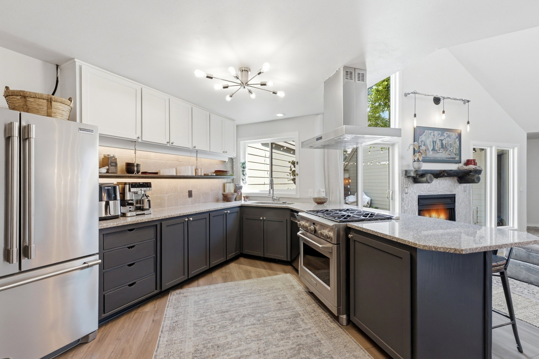 Contemporary kitchen featuring a stainless steel refrigerator, stainless steel range with hood, granite countertops, two-tone cabinetry with upper white and lower charcoal finishes, and wood-finish flooring