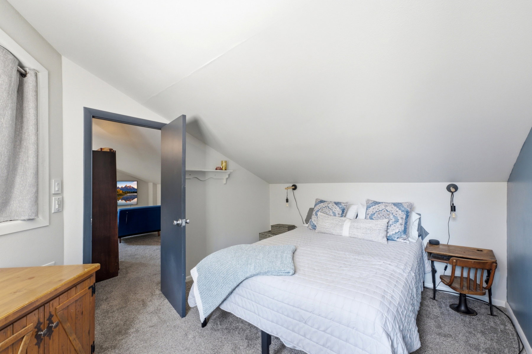 Carpeted room featuring a sloped ceiling, built-in wall sconces, and a window with a curtain rod