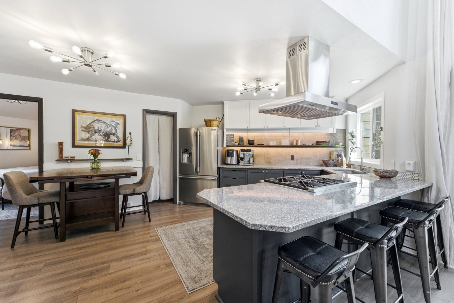 Open-concept kitchen featuring wood-finish flooring, a stainless steel range hood, an island with an integrated cooktop, stainless steel appliances, and under-cabinet lighting