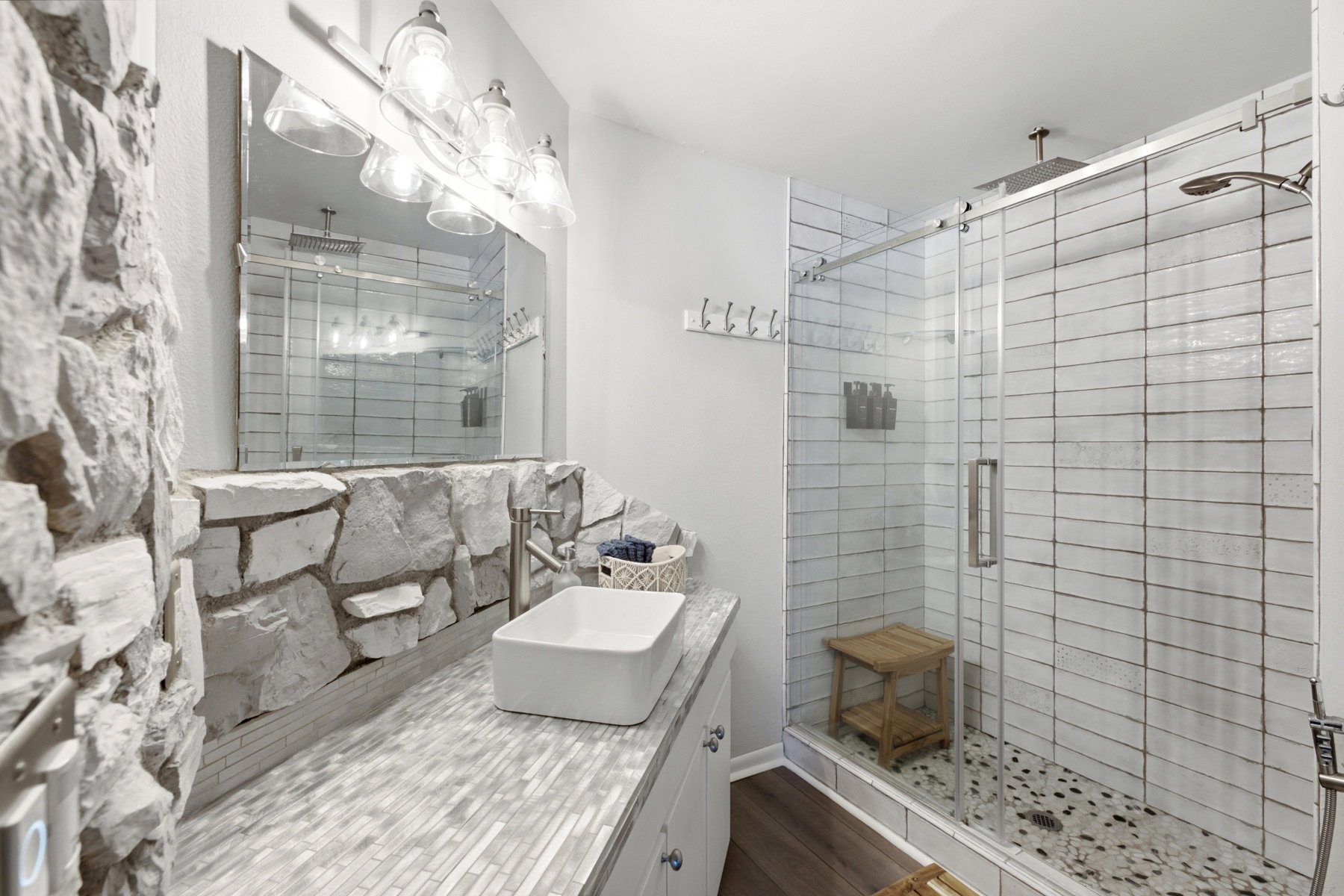 Stone accent wall with a vessel sink, mosaic tile countertop, and brushed nickel faucet