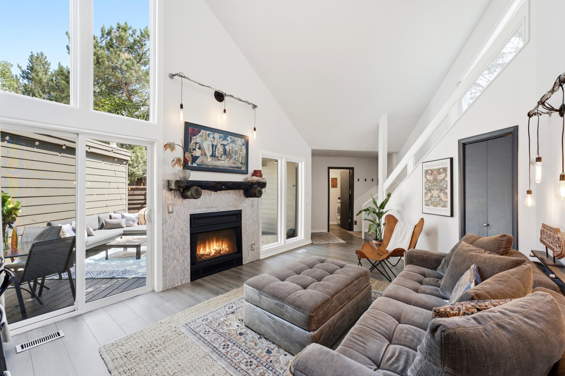 Vaulted ceiling living room featuring a tiled fireplace with wood mantel, light wood-finish flooring, and a sliding glass door opening to an outdoor patio
