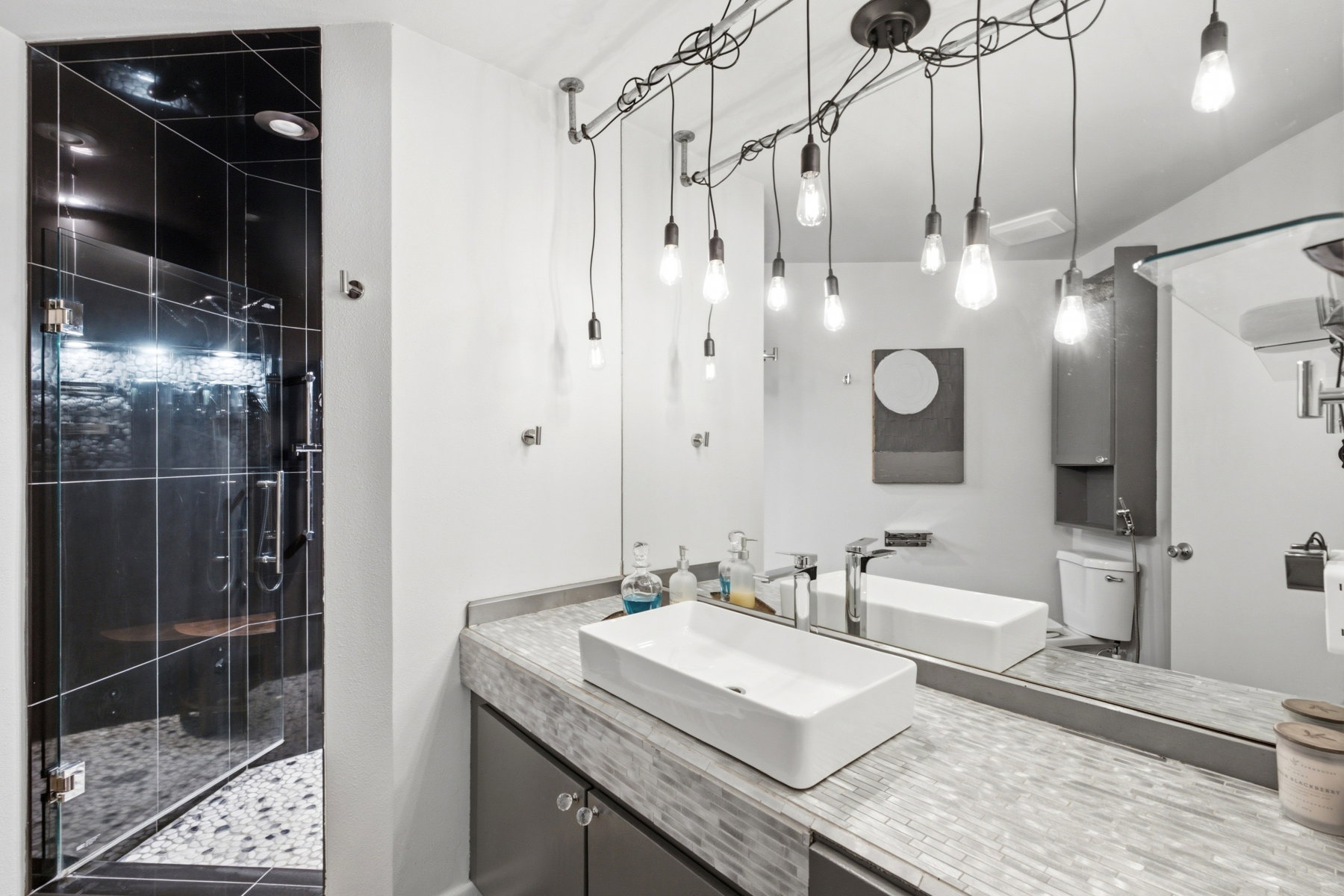 Contemporary bathroom featuring a spacious glass-enclosed shower with dark tile and pebble flooring