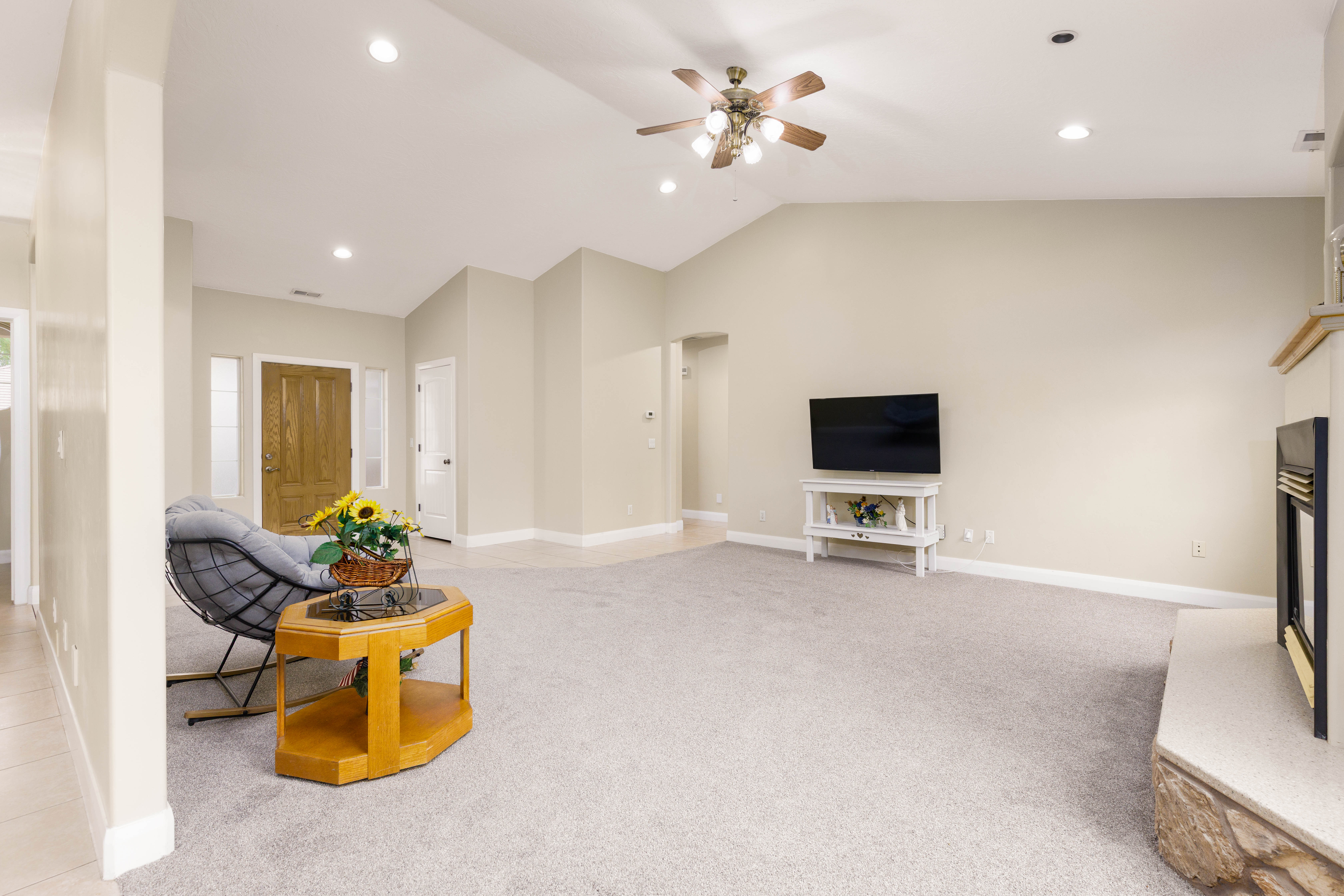 Spacious living area featuring vaulted ceilings, recessed lighting, ceiling fan, fireplace with stone surround, and light-toned carpet flooring