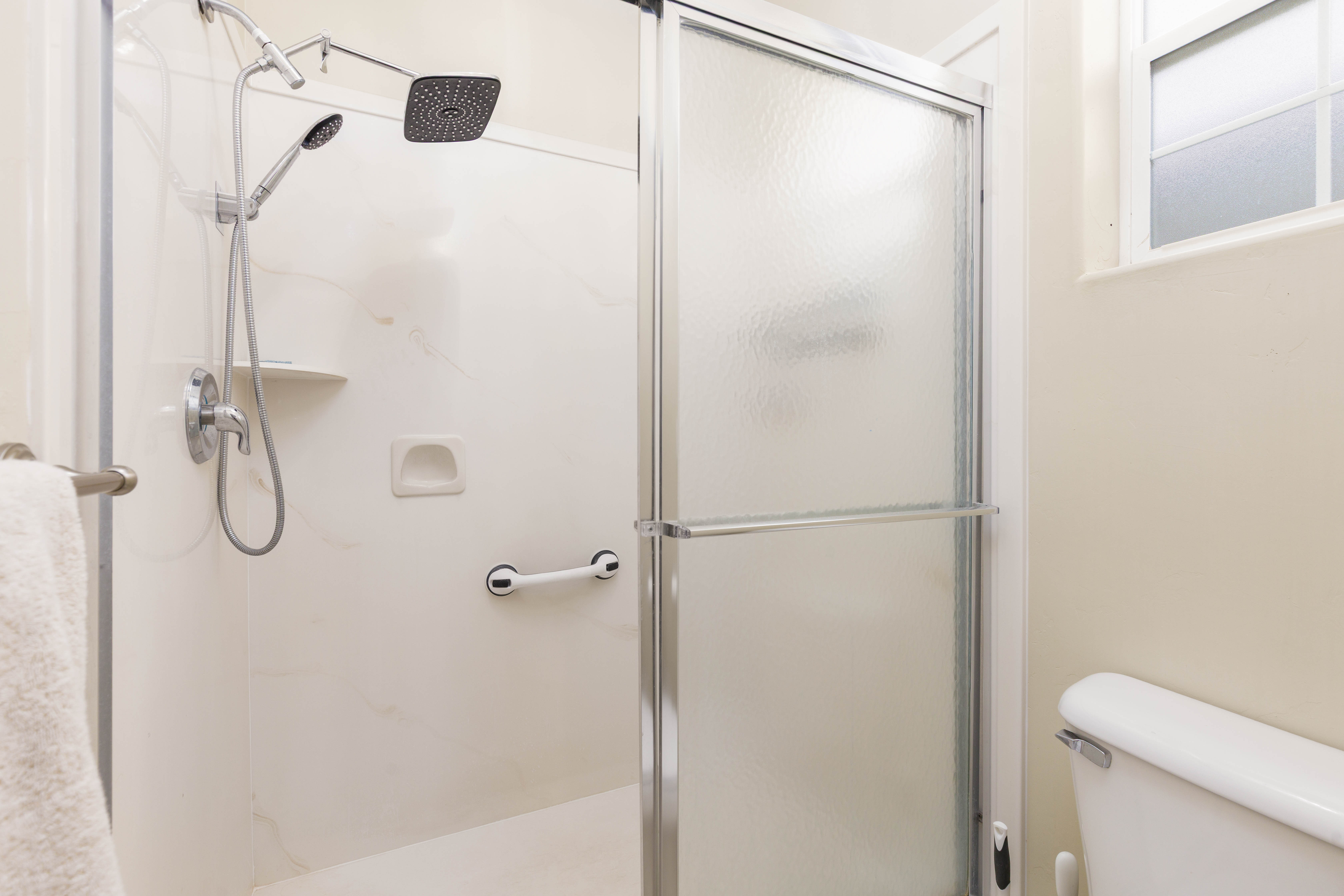 Walk-in shower with a glass enclosure, a handheld shower fixture, and a square rain showerhead