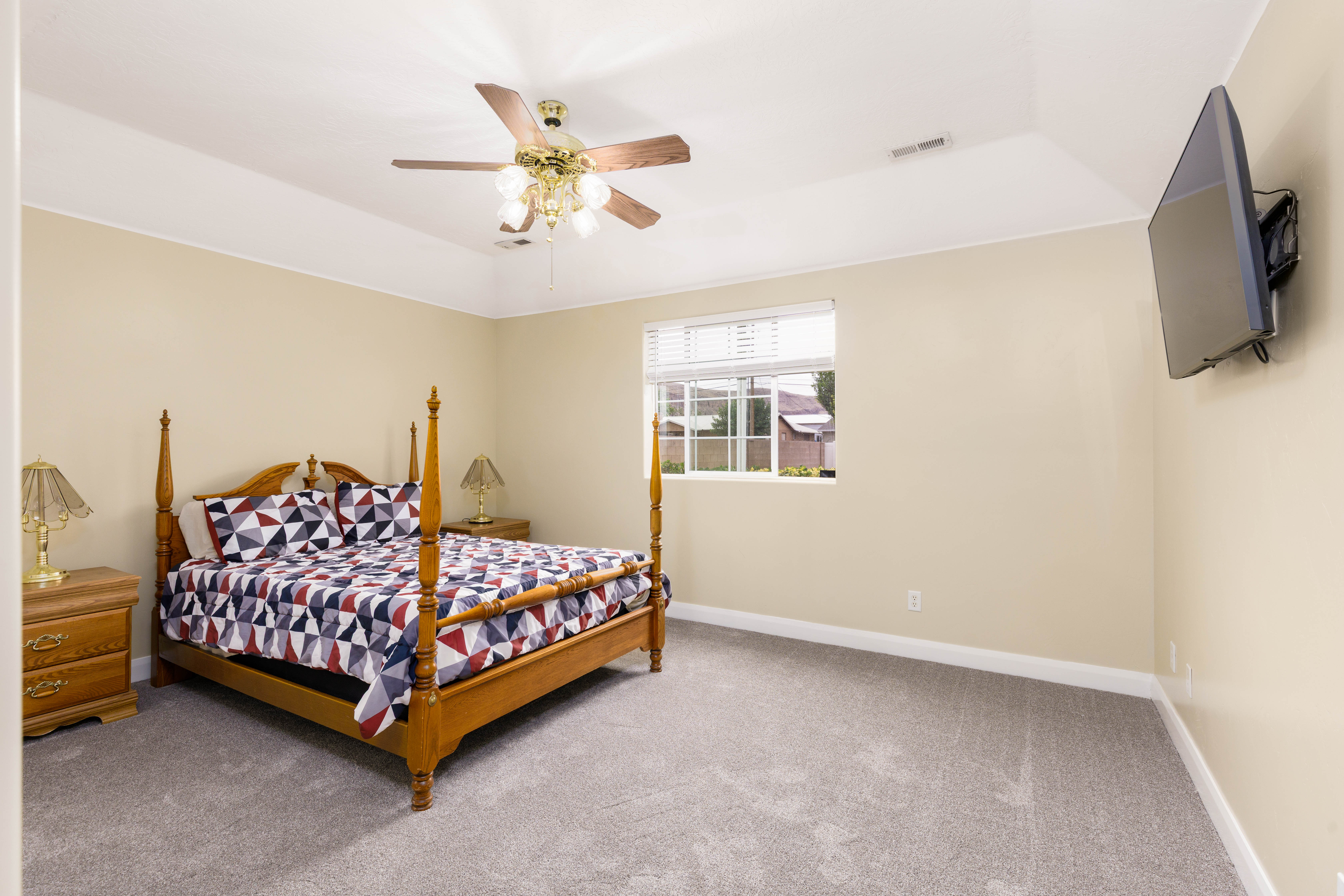 Spacious bedroom featuring neutral wall tones, plush gray carpeting, a tray ceiling, and a ceiling fan with integrated lighting