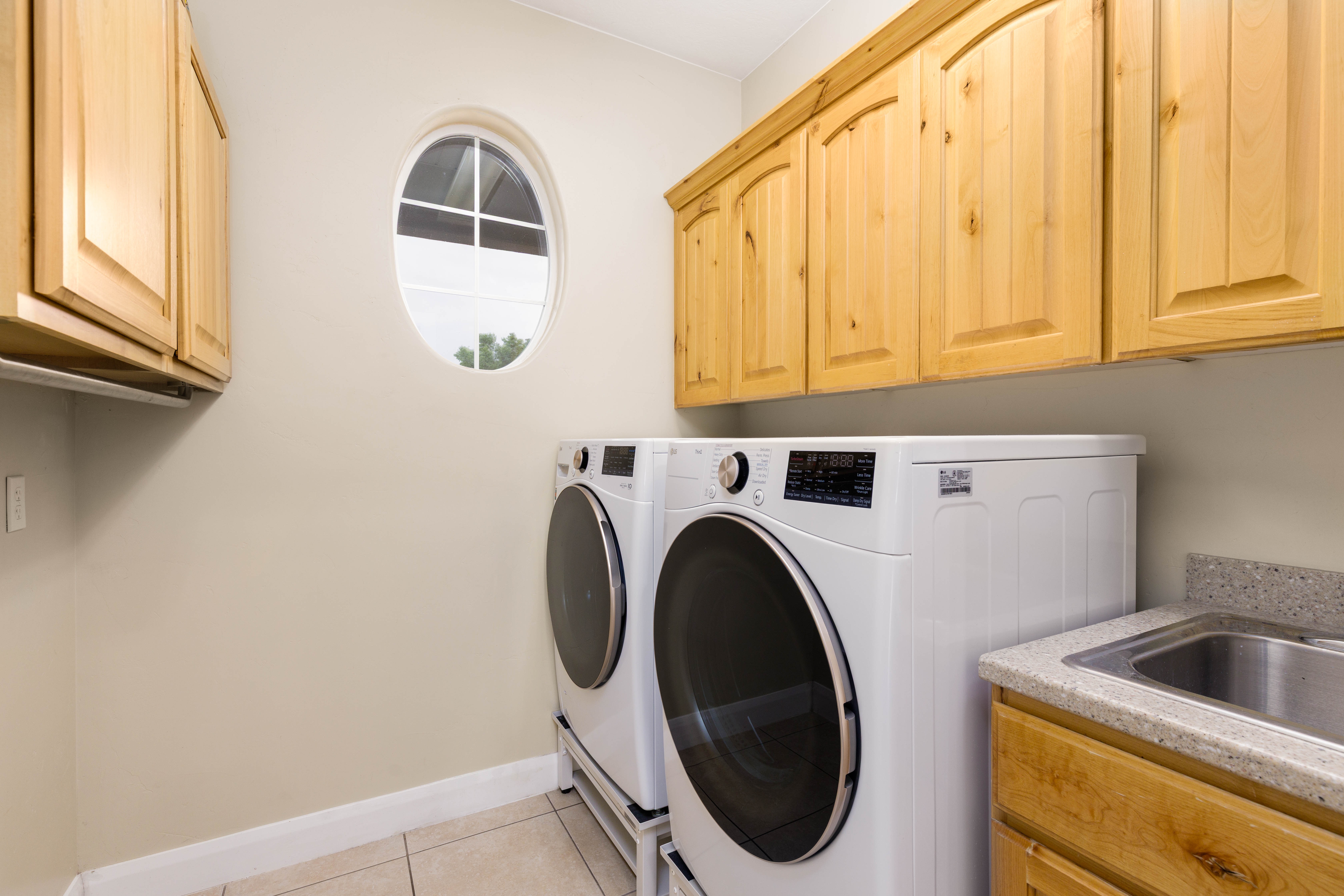 Utility room featuring a built-in sink with a speckled countertop, natural wood cabinetry, and an oval window